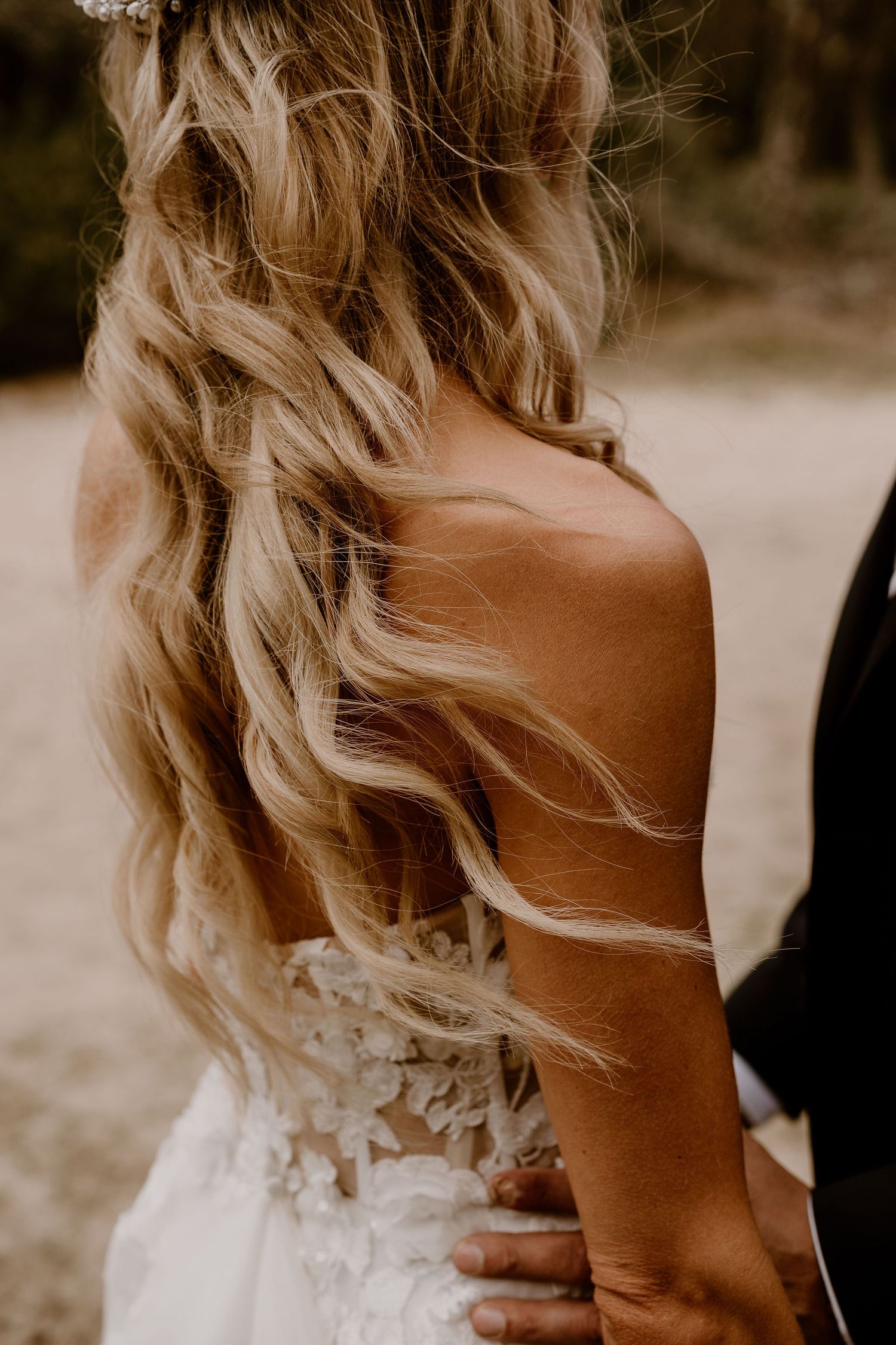 Elegant bridal portrait showing flowing blonde wavy hair and lace detail on the back of a white wedding dress.