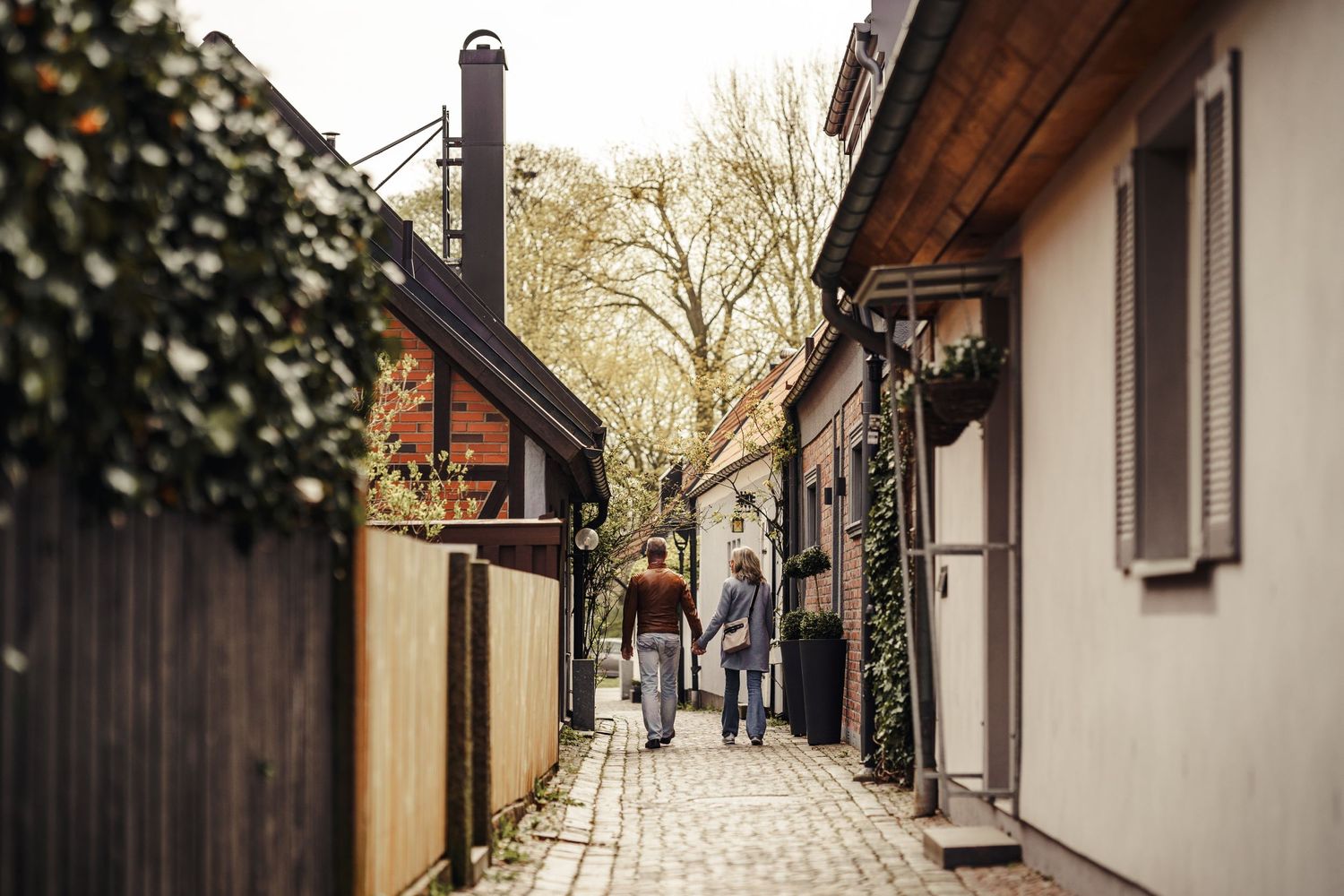 A person walks down a charming narrow cobblestone alley between rustic buildings with wooden details and window shutters.