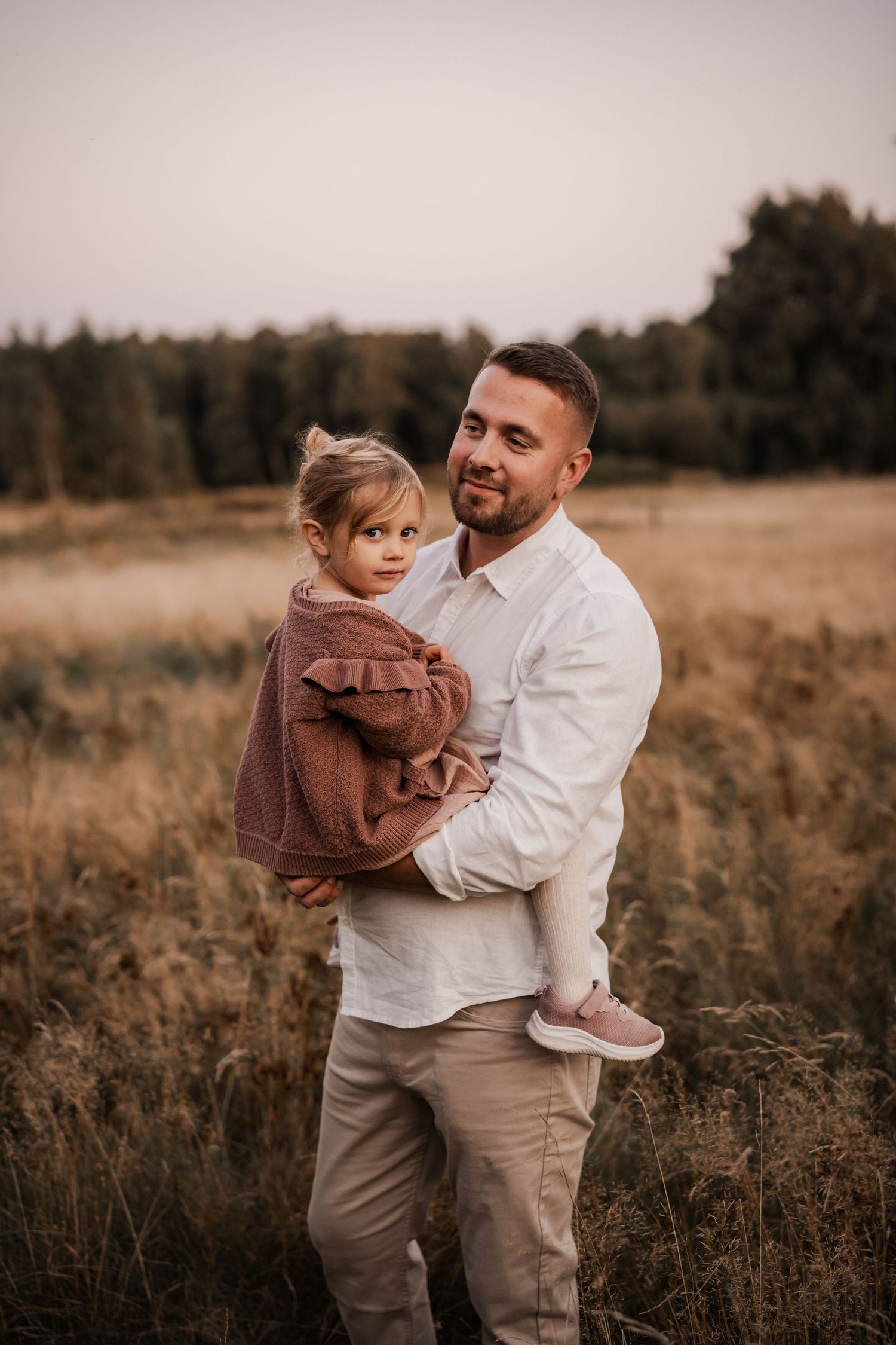 A parent and child share a tender moment in a golden field at sunset with trees in the background.