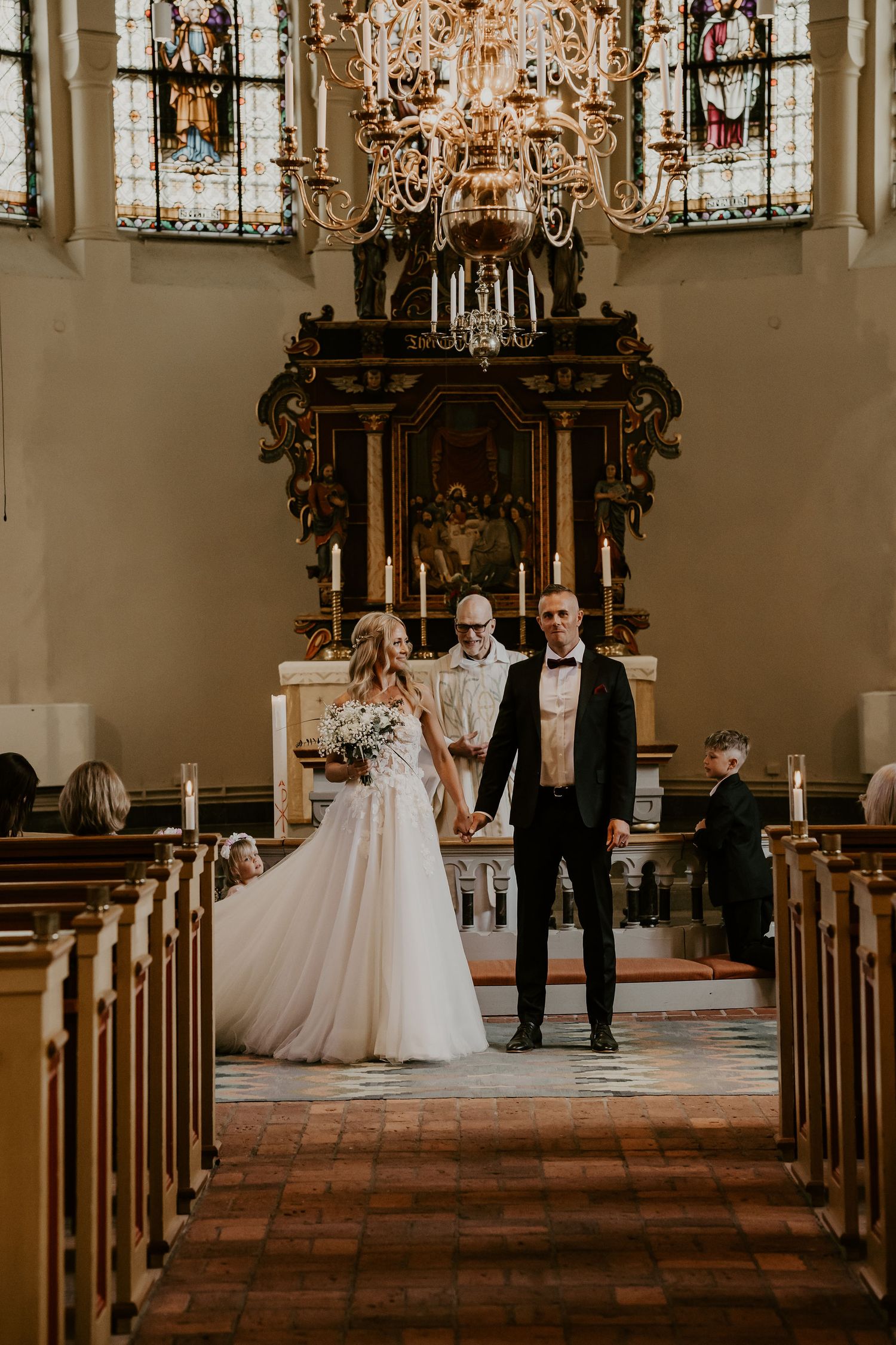 Wedding ceremony in a historic church with ornate chandelier and stained glass windows, featuring a traditional aisle setup.