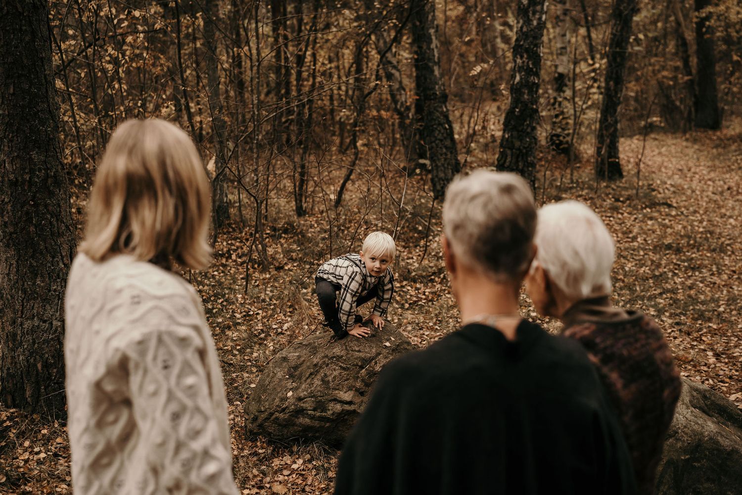 Family gathering in an autumn forest with fallen leaves and natural lighting.