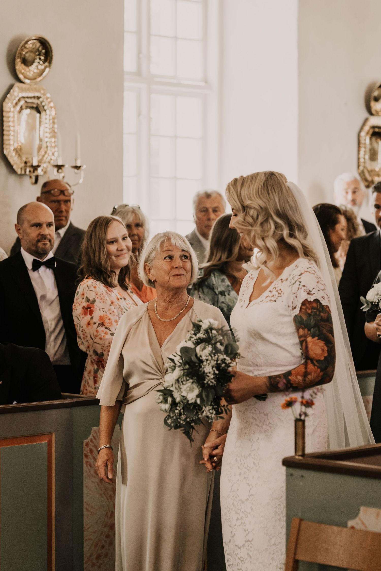 A tender moment captured at a formal wedding ceremony inside a church with ornate wall sconces and elegant decor.