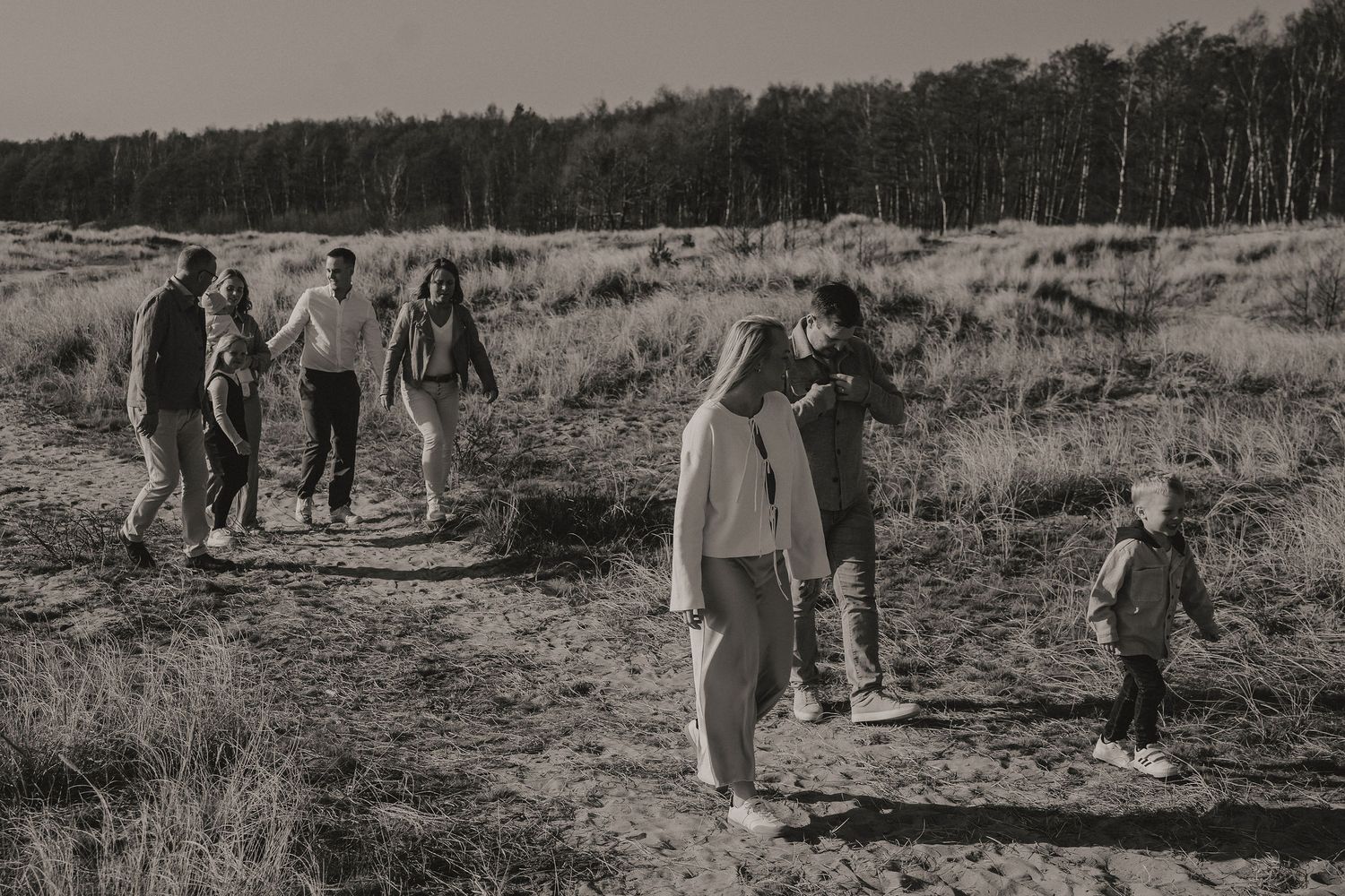 A group of people hiking together along a nature trail through a scenic open field in black and white photography.