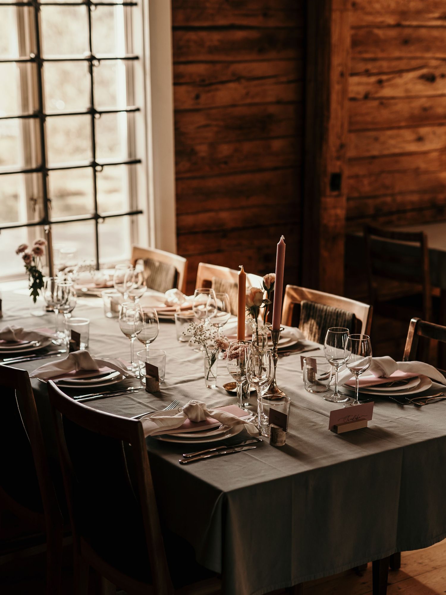 Rustic dining table set with elegant place settings, candles, and dried flowers in a wooden cabin interior.