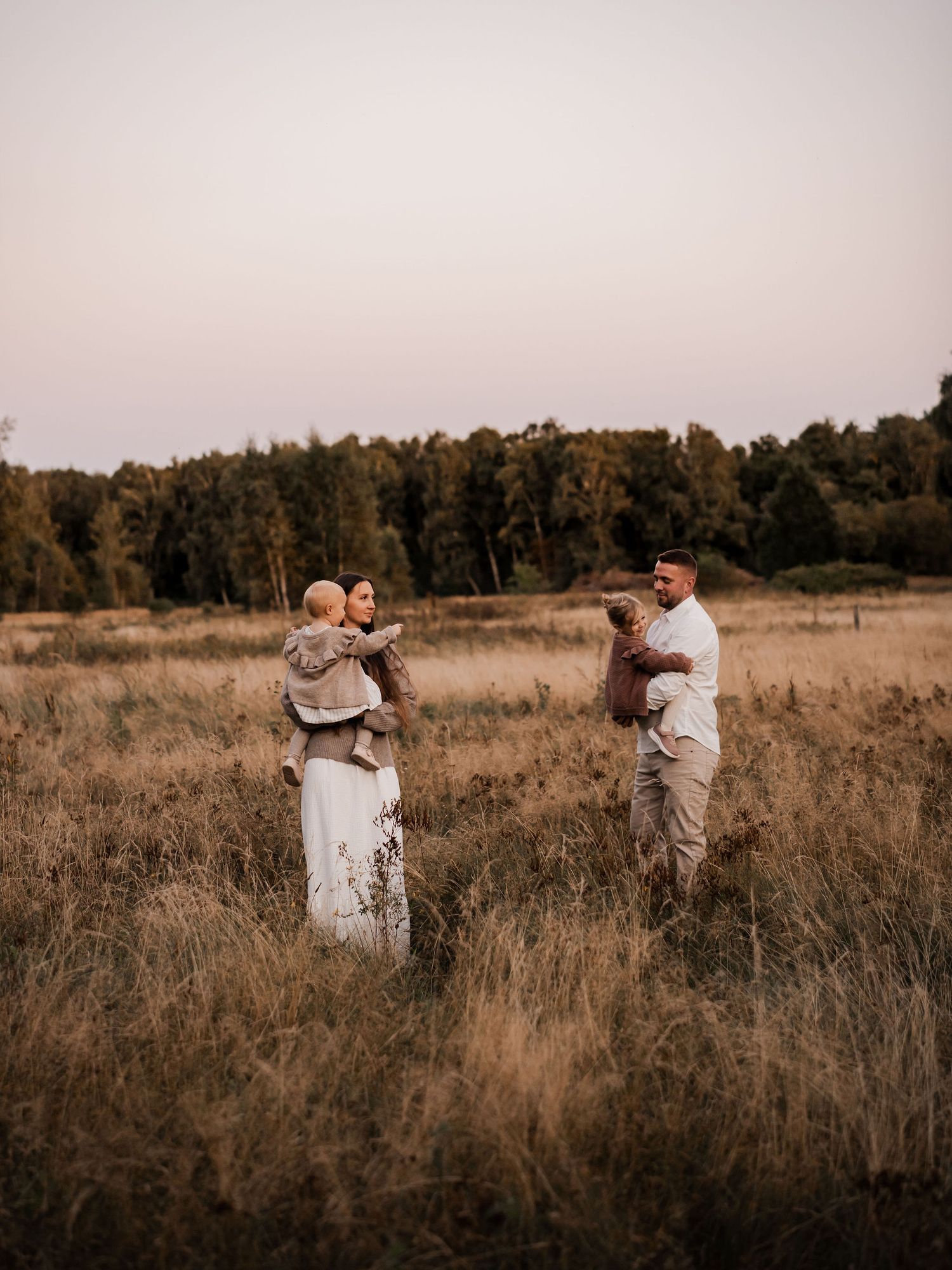 Family stands together in a rustic field during golden hour sunset.