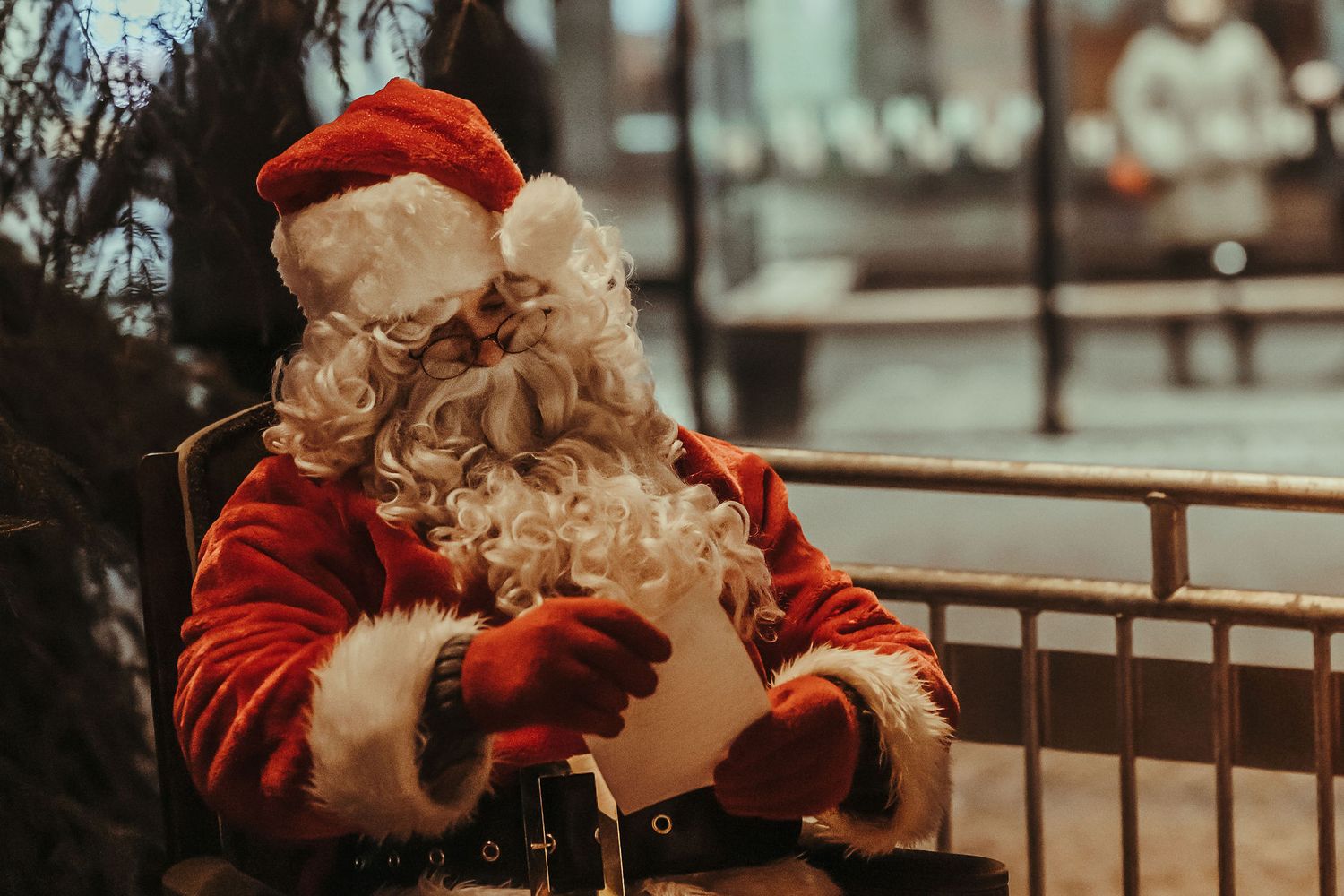 A festive figure in a traditional red suit and white beard sits outdoors in wintertime.
