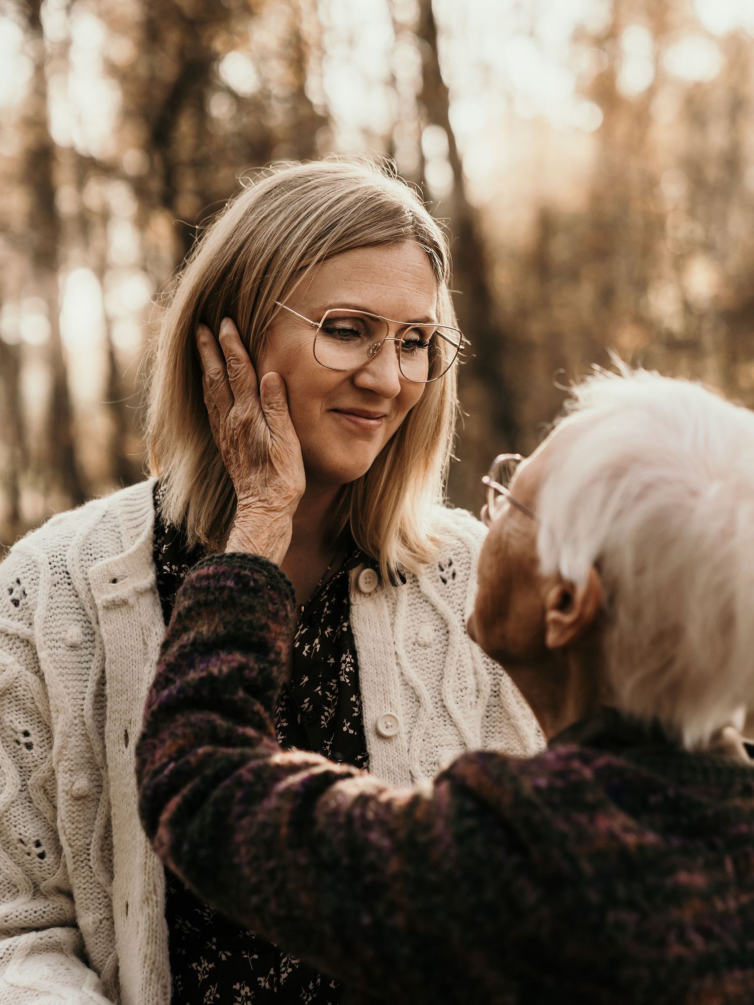 Two people sharing a tender moment in autumn forest lighting with one wearing glasses and a cream cardigan.
