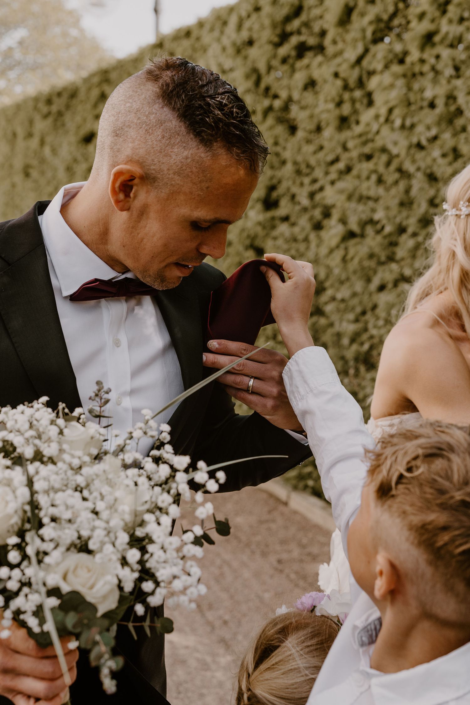 A touching wedding moment with a groom in a dark suit and bowtie as delicate baby's breath bouquet fills the frame.