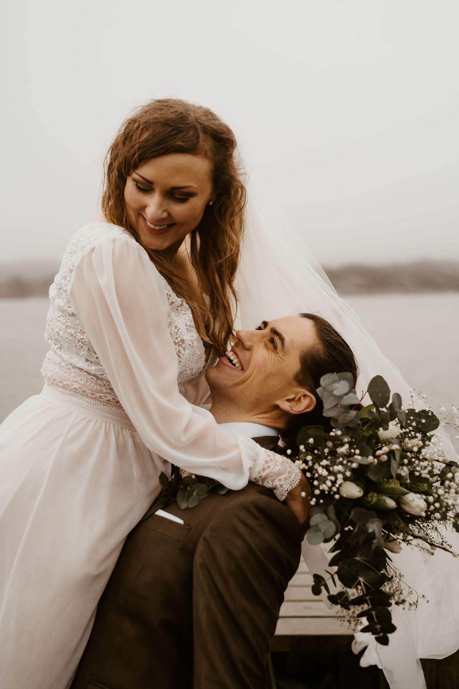 A romantic wedding moment captured outdoors as a loving couple embraces with baby's breath bouquet.