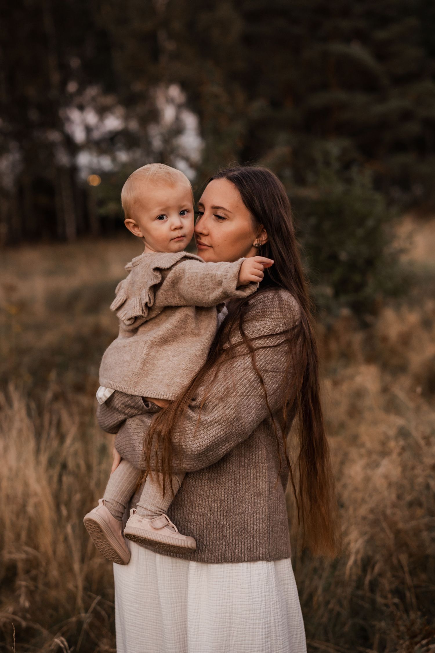 Tender moment between parent and young child in matching neutral tones against autumn field.