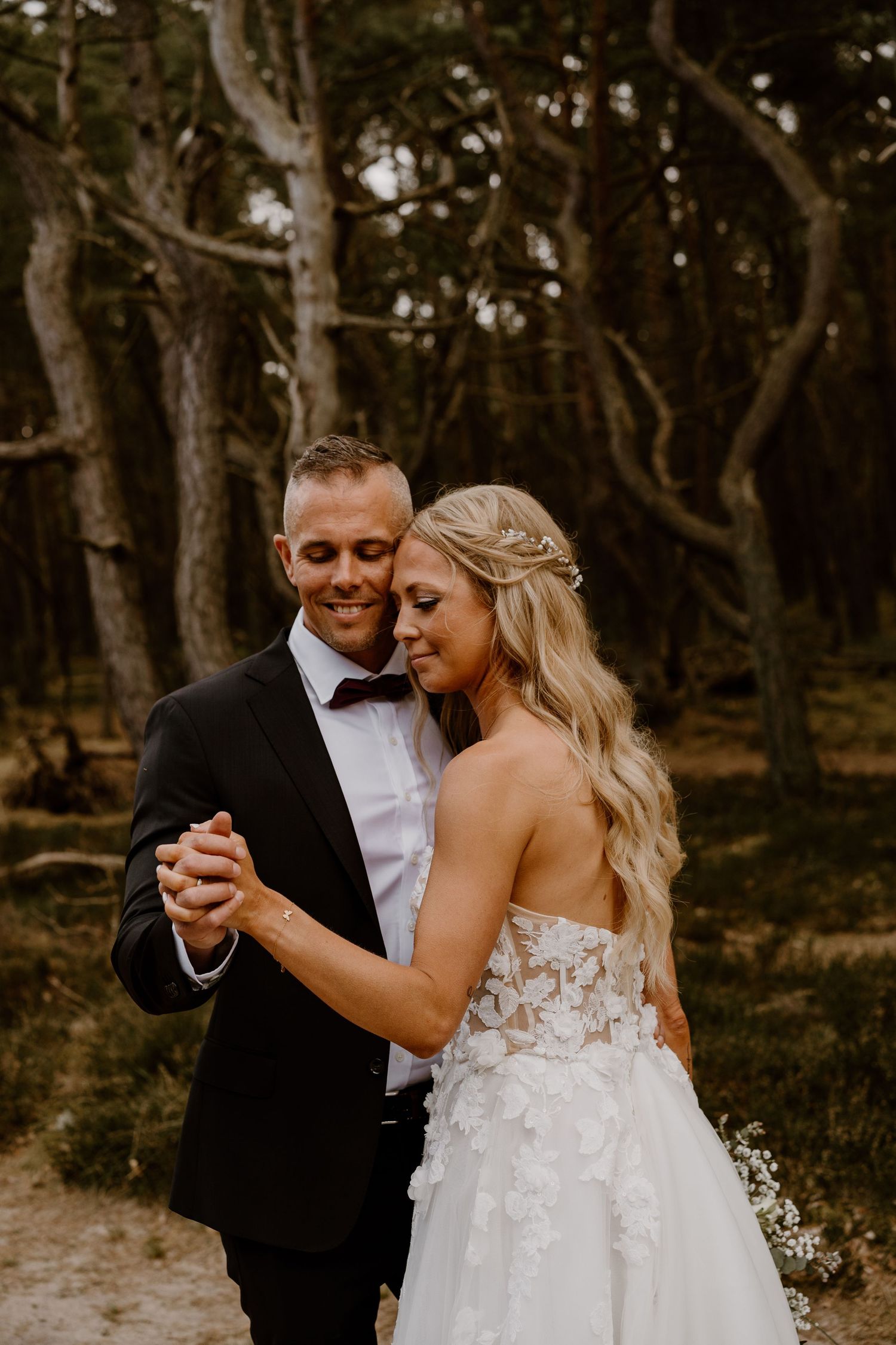 A couple shares an intimate dance in a woodland setting, with the bride wearing a flowing white gown with floral details.