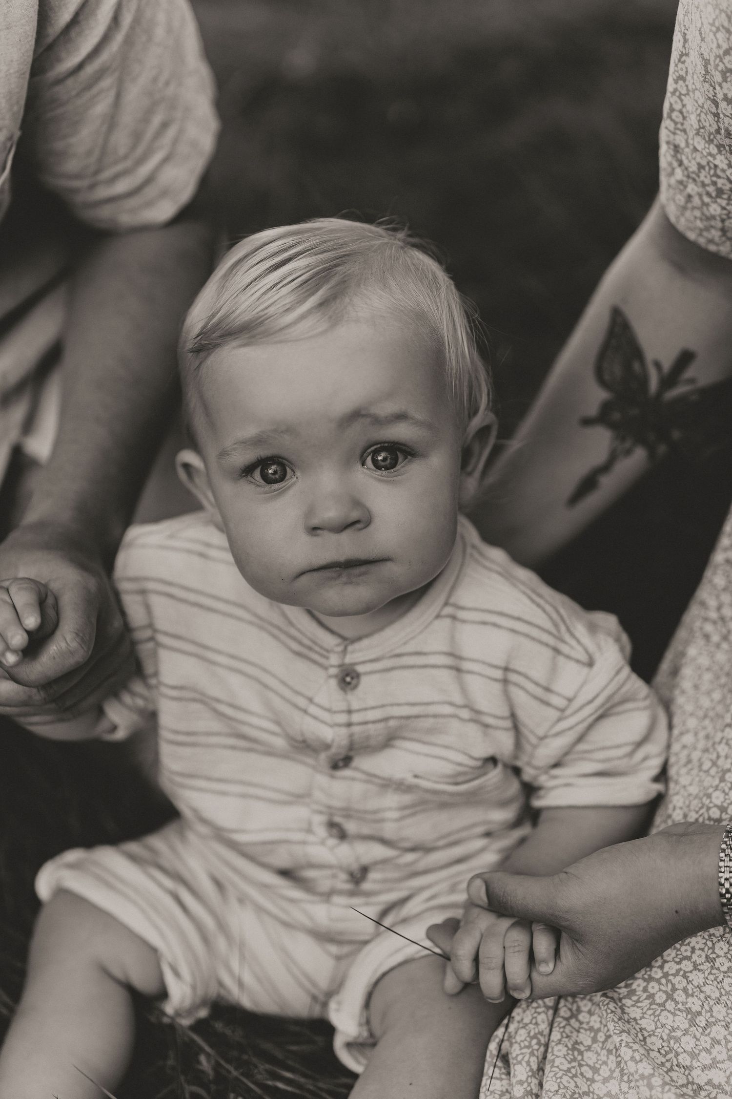 Close-up black and white portrait of a baby in striped clothing held by parents.
