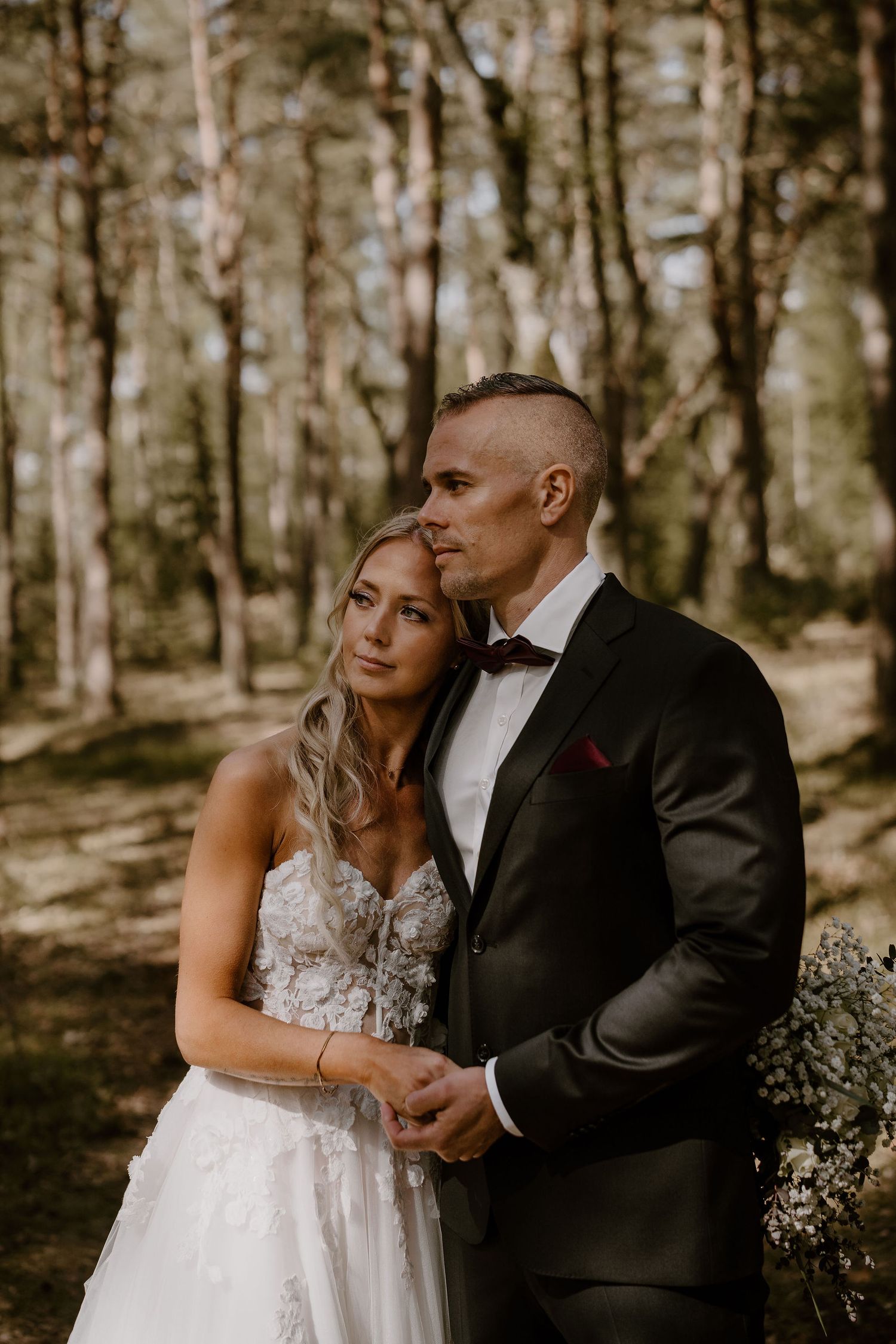 A couple shares an intimate moment in a sunlit birch forest, with the bride in a lace gown and groom in classic tuxedo.