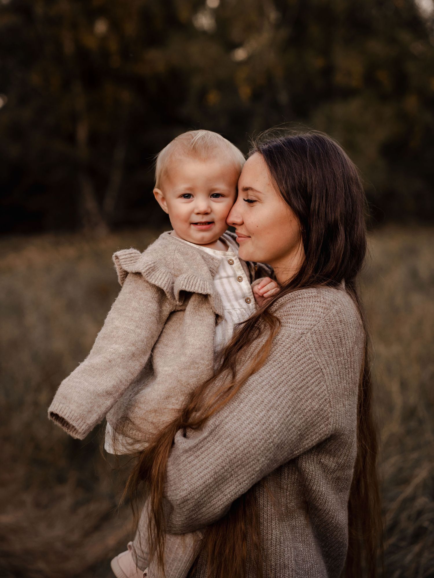 A mother in a knit sweater holds and cuddles with her baby in a outdoor autumn setting.