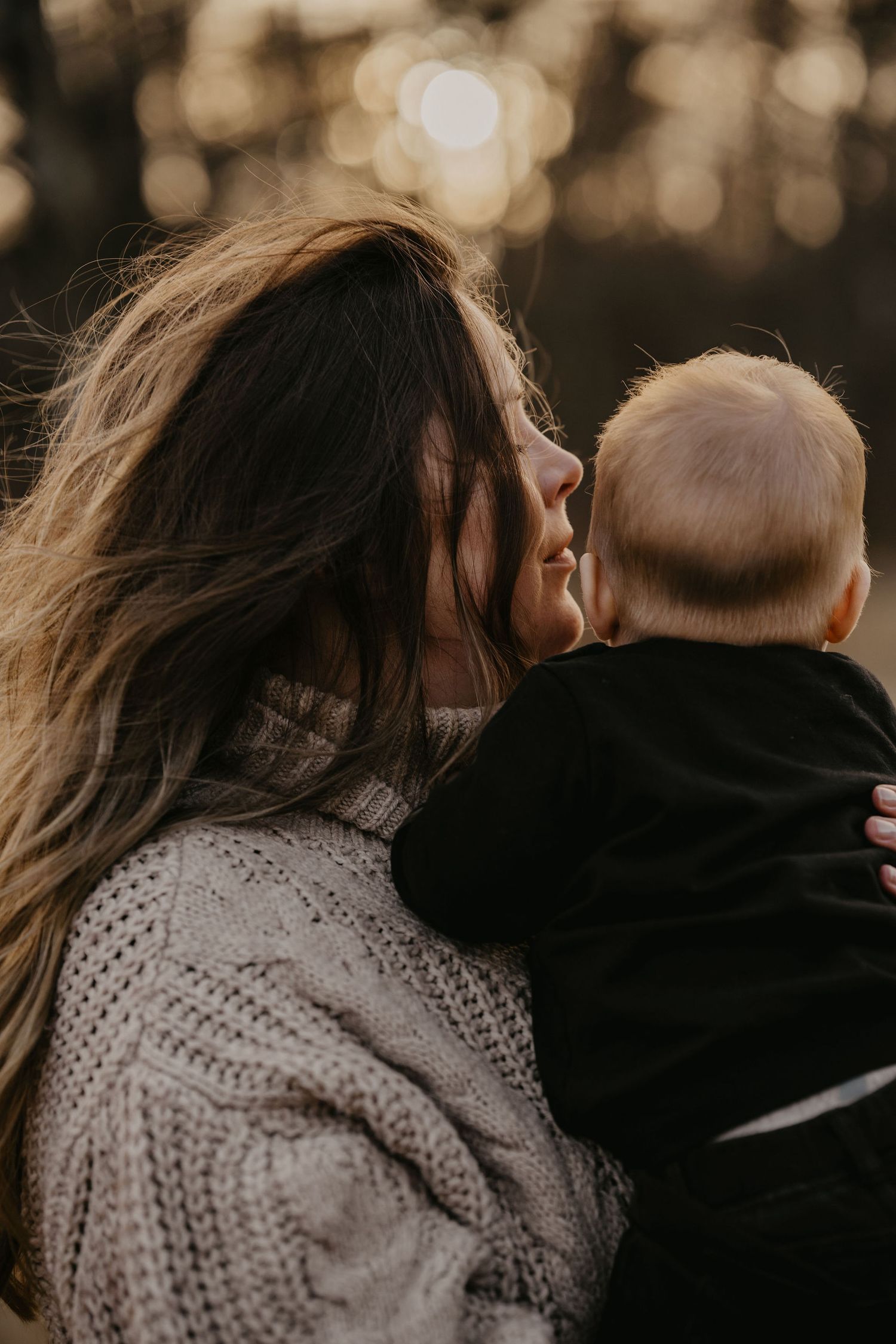A tender moment captured in warm light as a parent in a knit sweater holds their baby against a bokeh background.