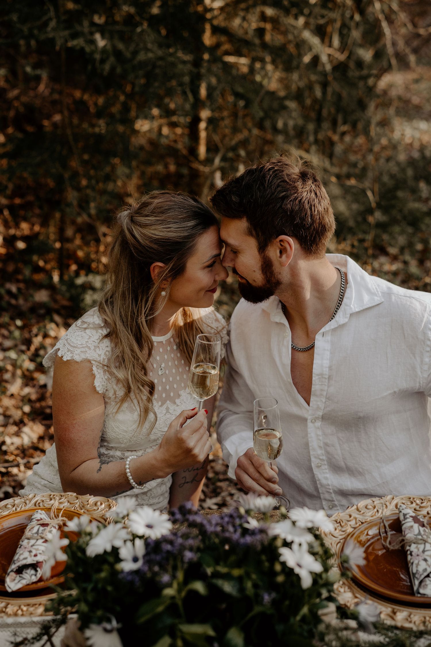 Romantic couple having champagne at an outdoor picnic with flowers and rustic decor at sunset.