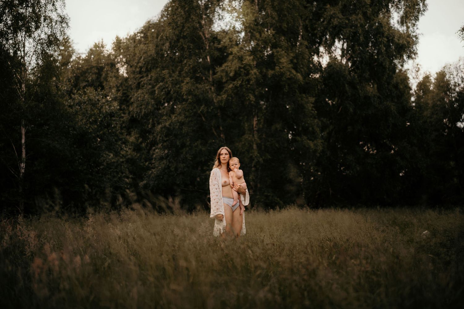 Couple standing together in a serene field with birch trees at golden hour.