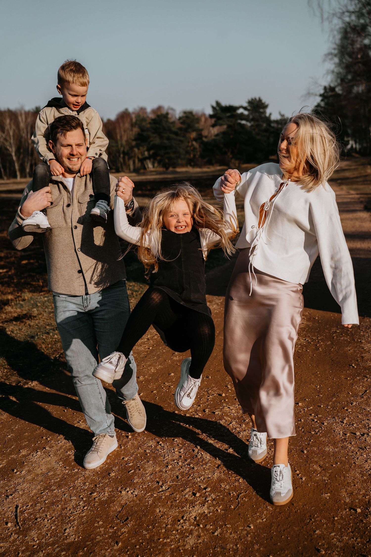 Family enjoying playful moment while walking outdoors together on sunny autumn day at park.