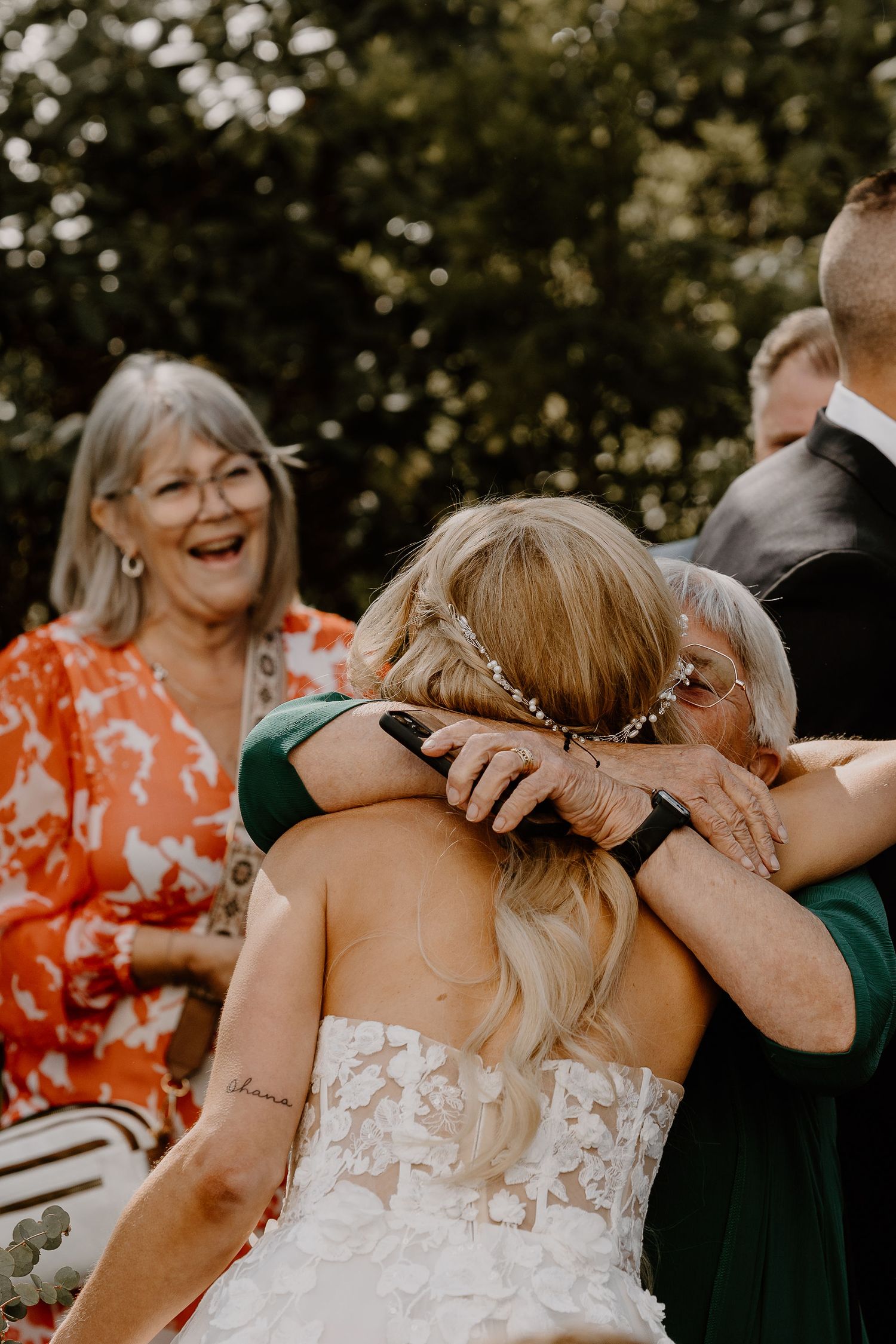 A candid moment of joy and emotion at an outdoor wedding celebration with family members embracing and laughing.