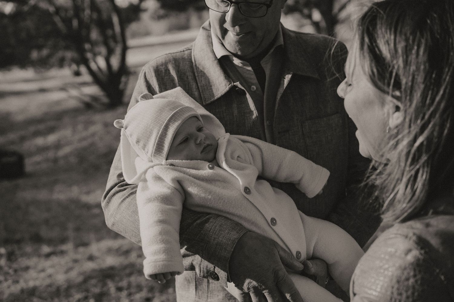 Black and white portrait of a couple sharing a tender moment with their baby outdoors.