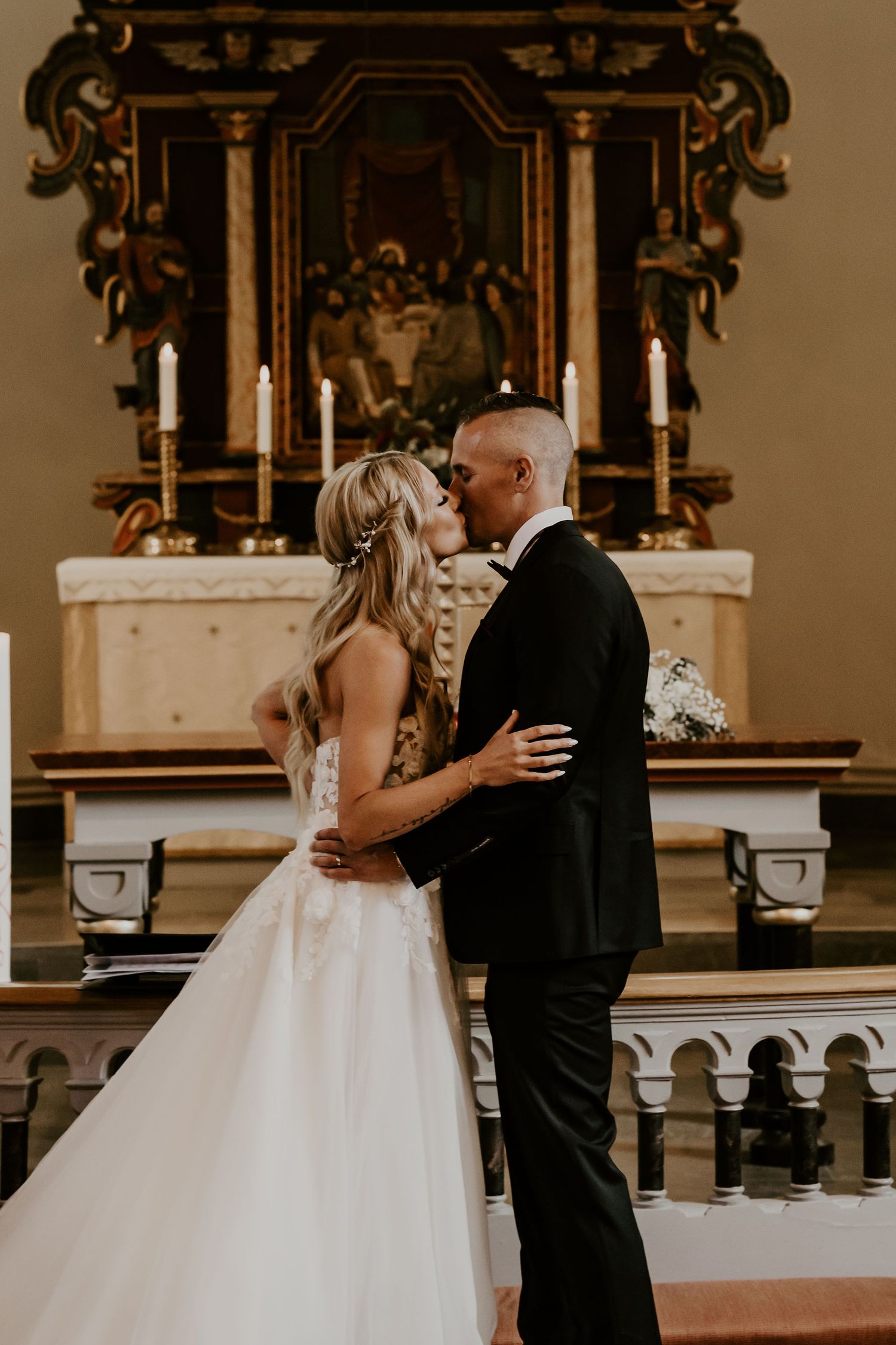 Intimate wedding moment captured in front of an ornate altar with candles and decorative religious artwork.