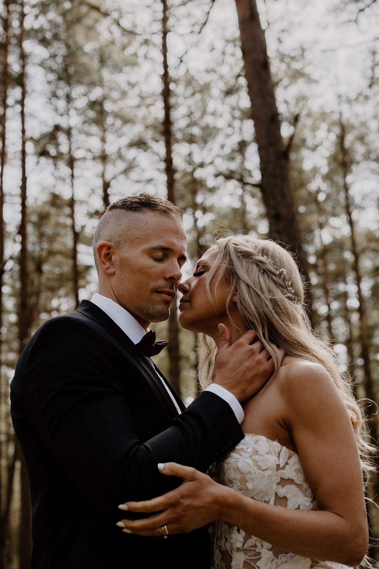 Romantic wedding photograph in a forest setting with couple in elegant attire sharing an intimate moment.