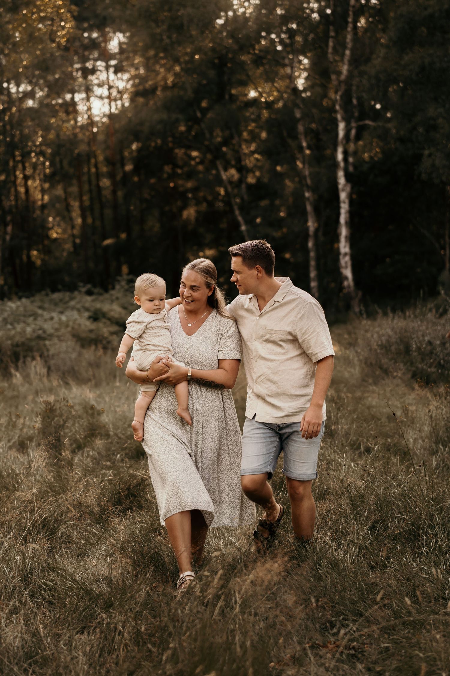 A family walking together through a sunny autumn field with tall grass and birch trees in the background.