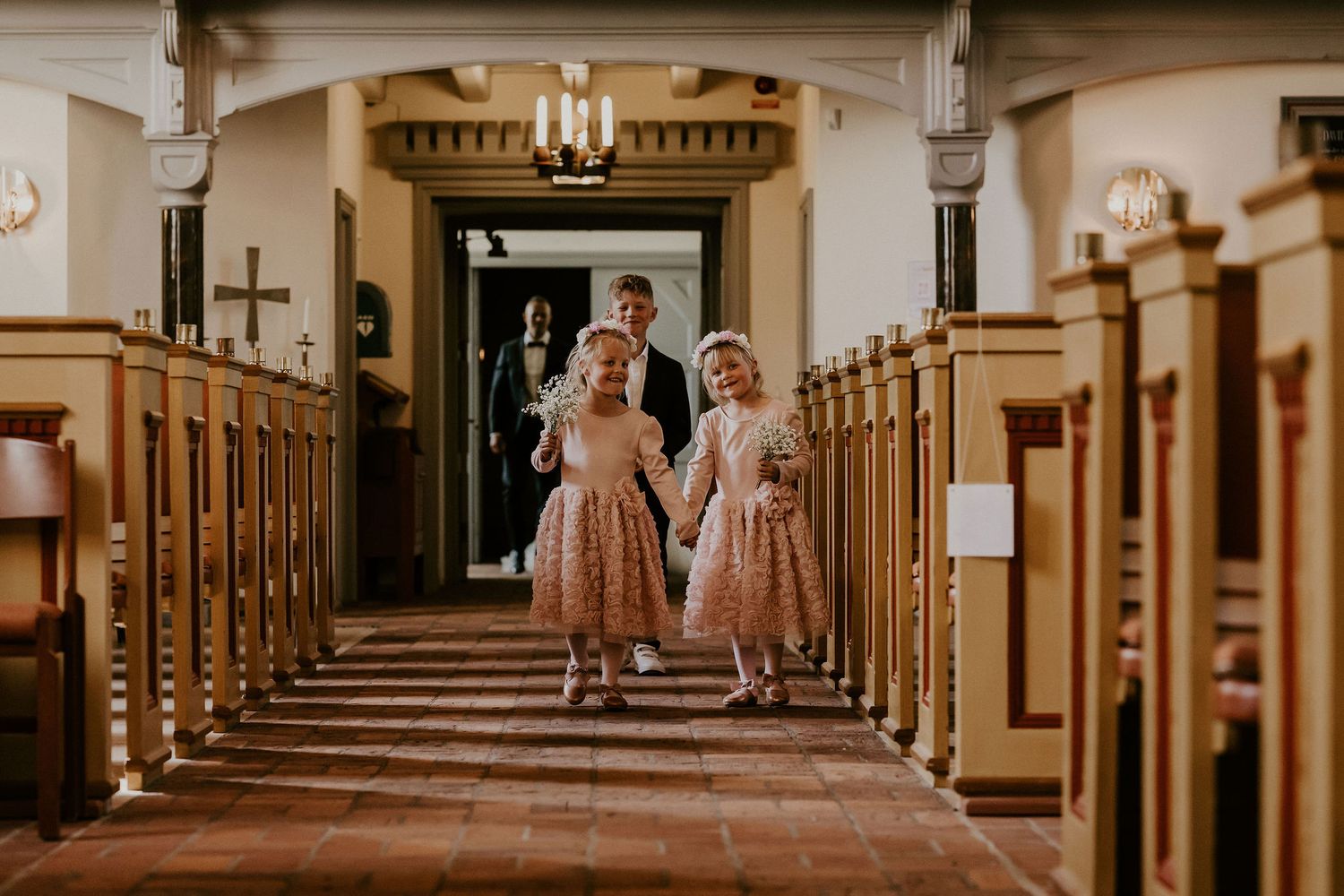 Two bridesmaids in pink dresses walking down a traditional church aisle with wooden pews.