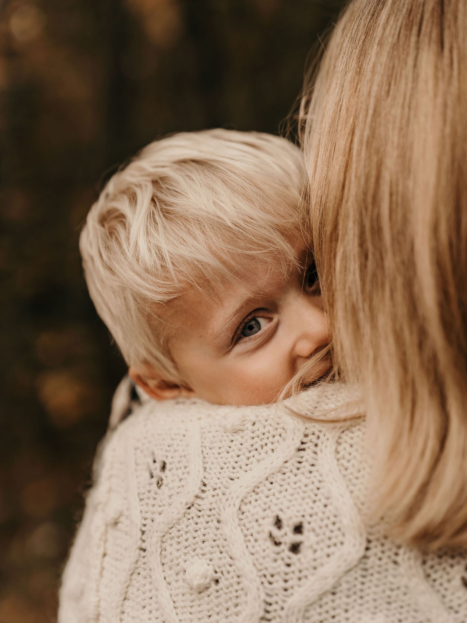 A child peeks over a shoulder wearing a cozy knit sweater in warm autumn tones.