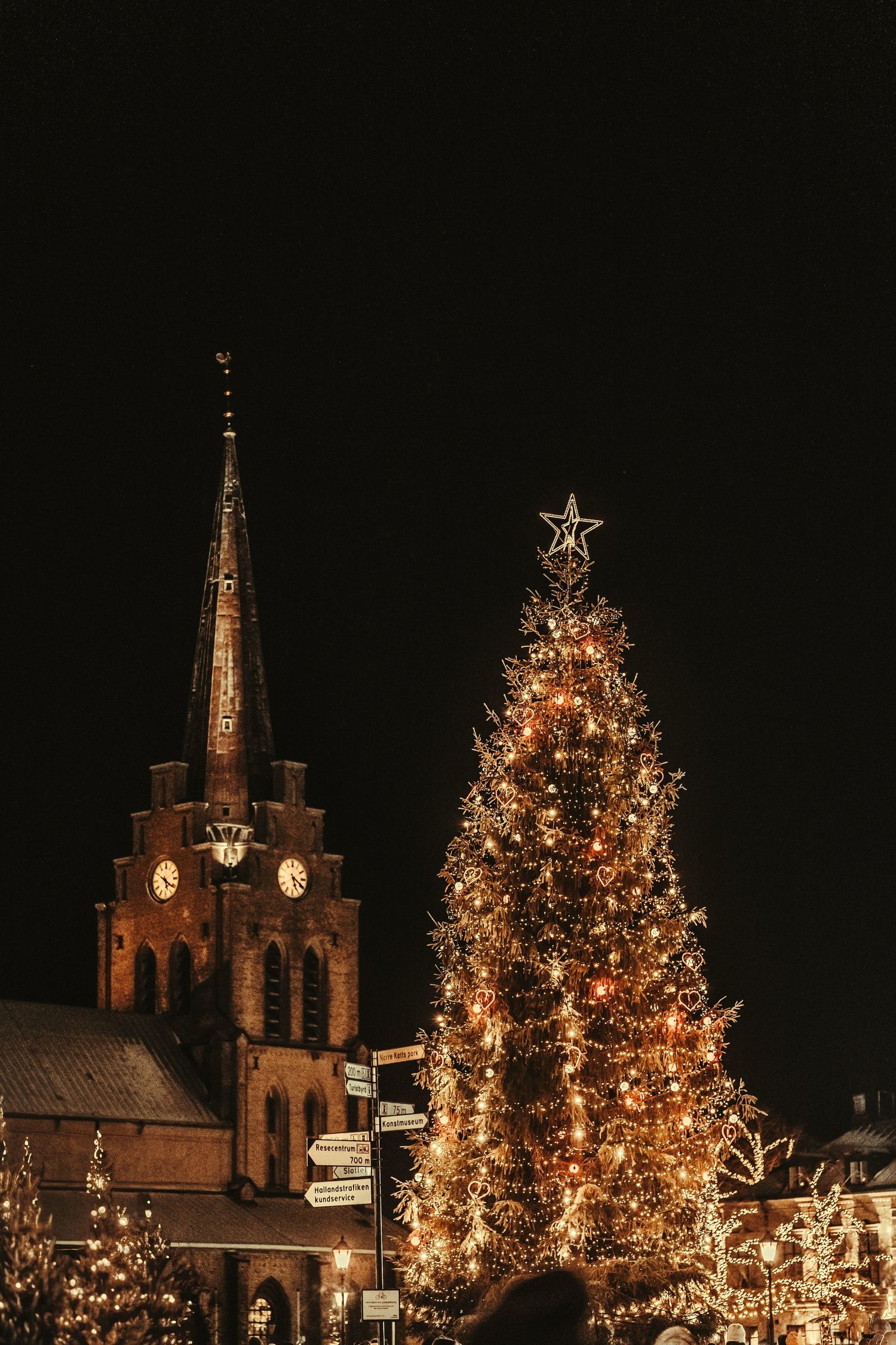 Illuminated Christmas tree next to a church spire at night with festive holiday lights glowing.