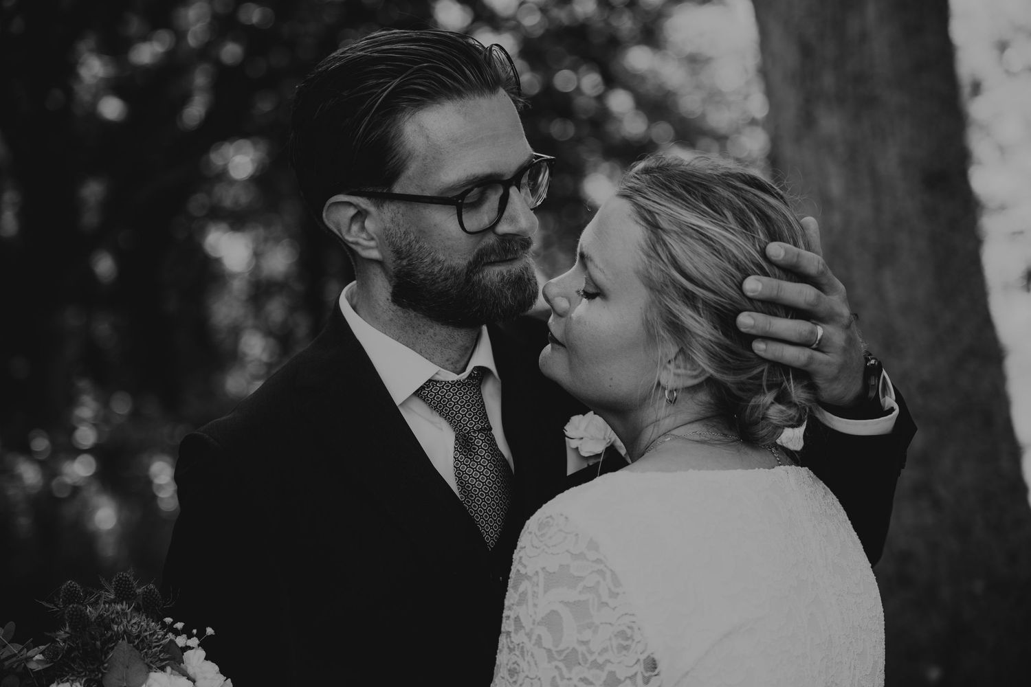 A couple shares a loving moment on their wedding day next to a lighthouse at sunset.