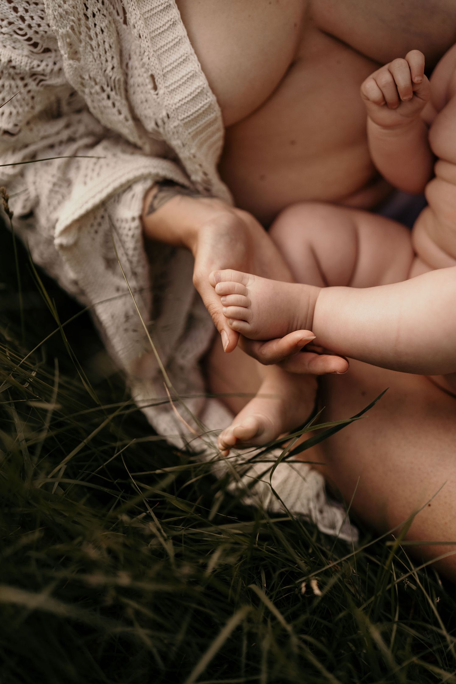 Close-up of tiny baby feet and hands on a knit blanket in natural outdoor setting.