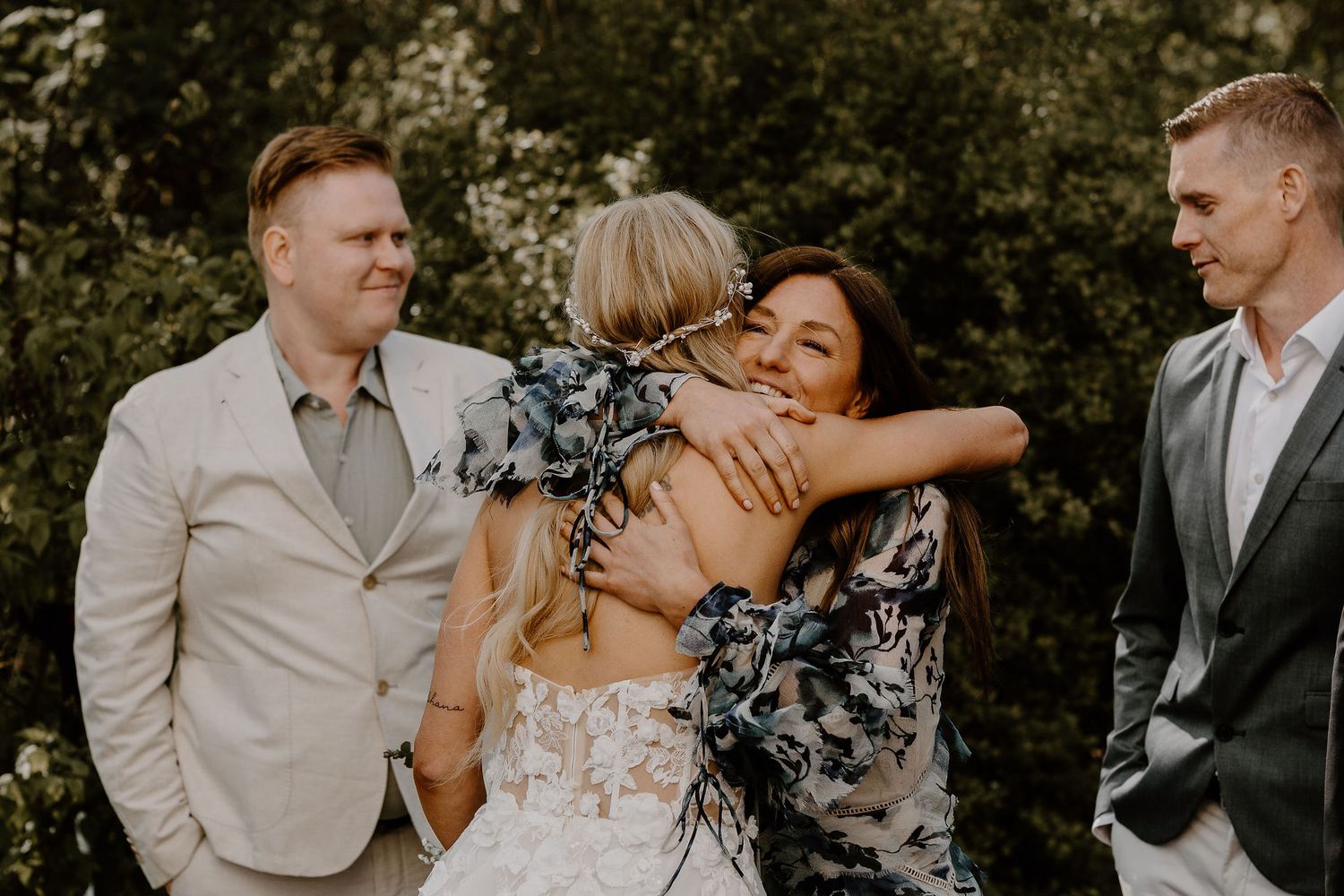 Happy wedding guests and bride sharing an emotional group hug during outdoor celebration.