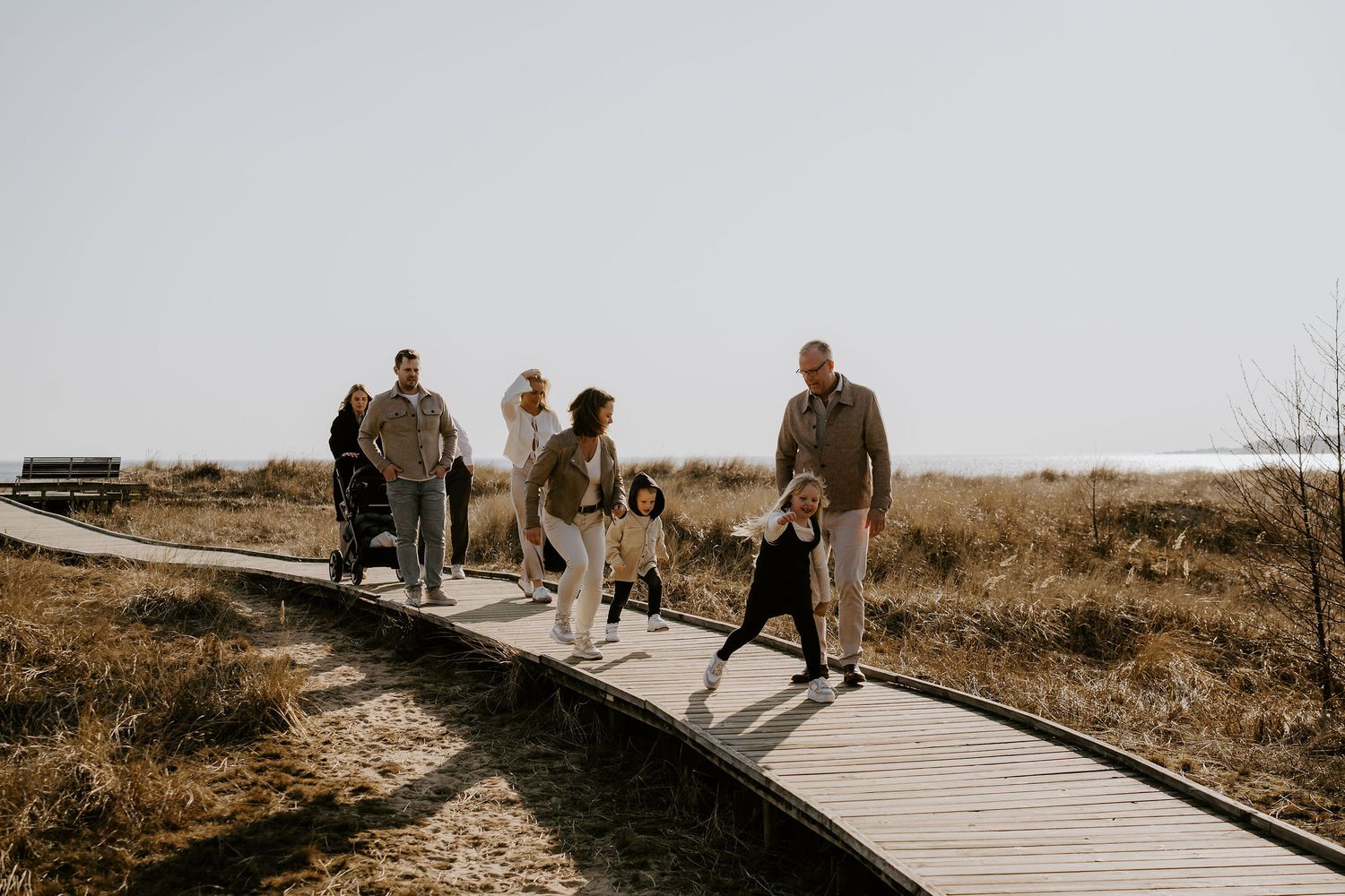 Group walking together on a wooden boardwalk path through a natural coastal area during golden hour.