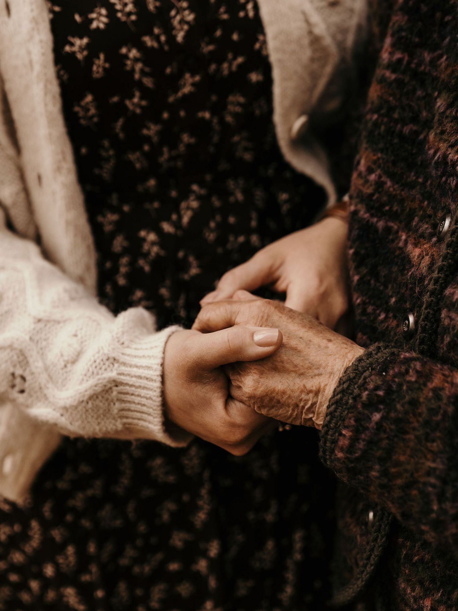 Close-up of hands clasping together, showing tender connection between generations wearing knit and textured fabrics.