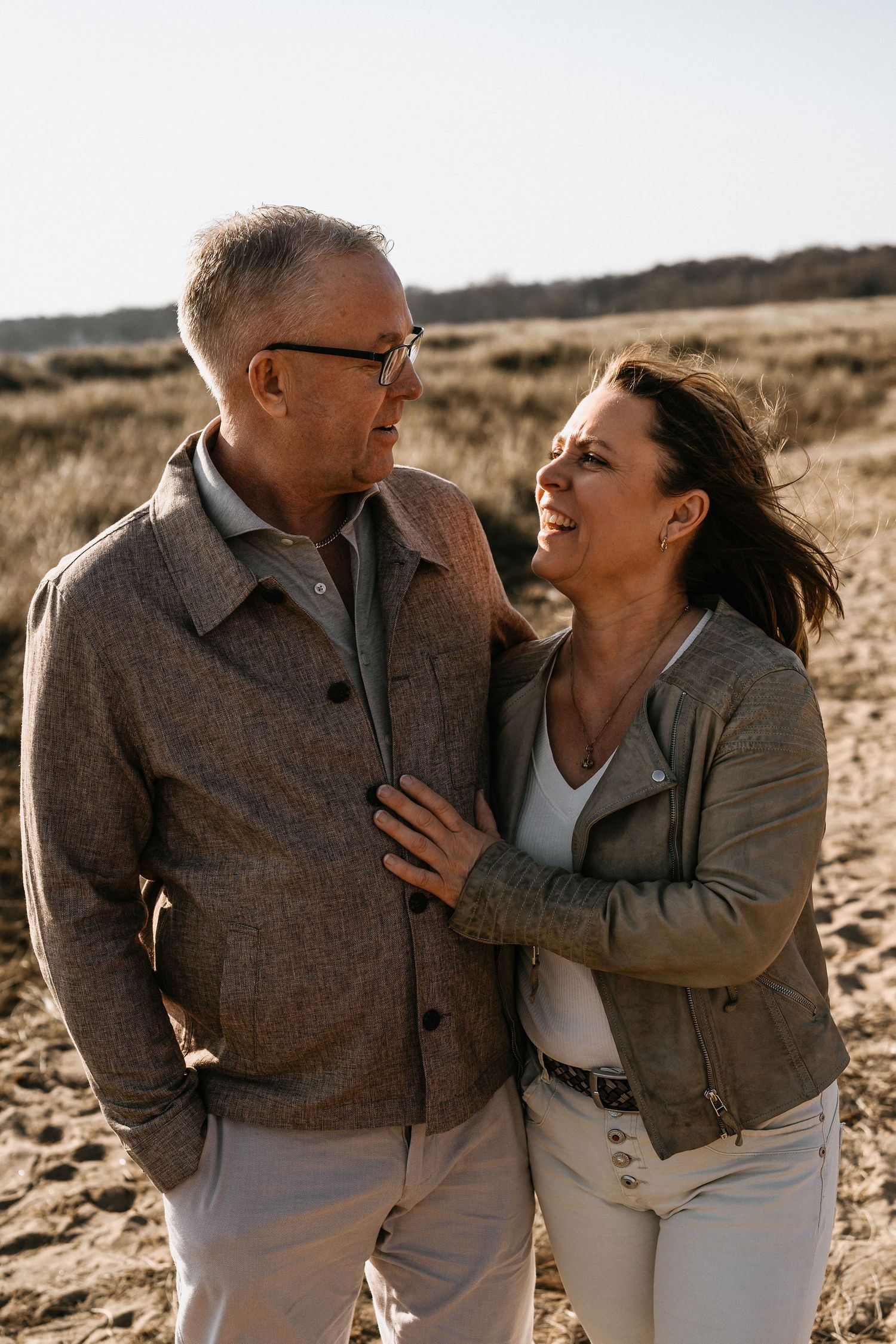 A loving couple shares a tender moment together while walking on sandy terrain at sunset.