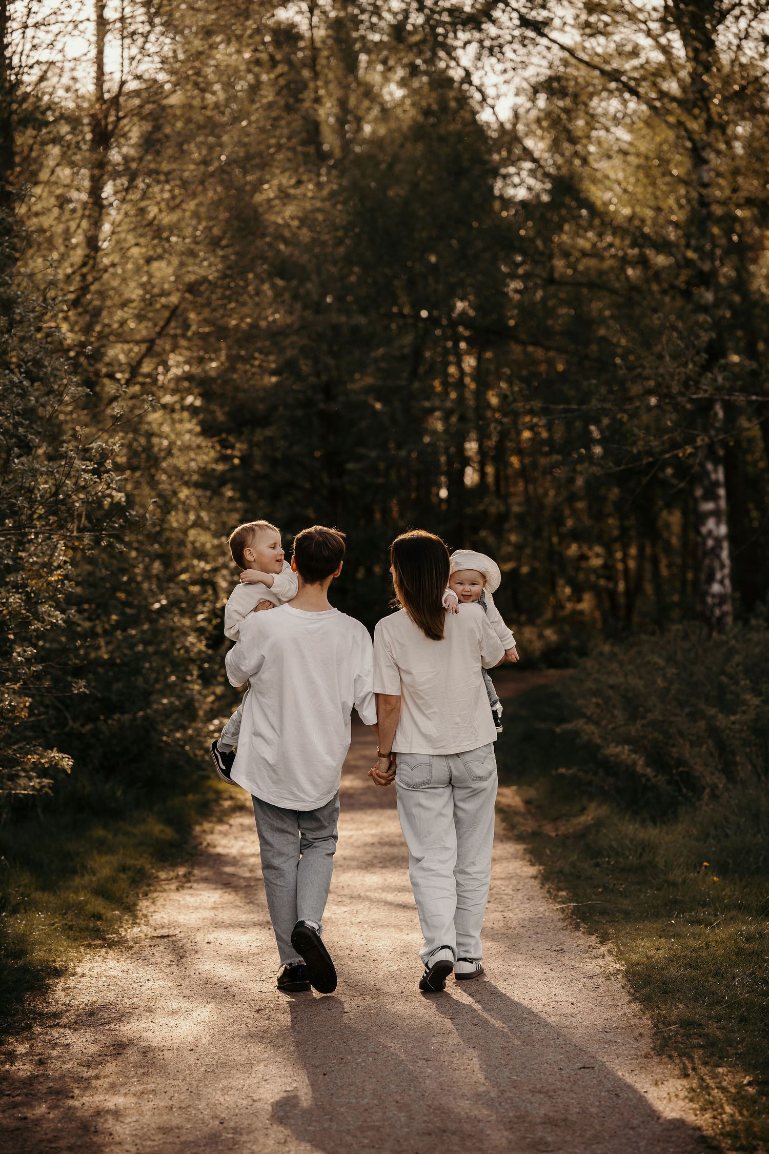 Two people in white clothing walking together on a sunlit forest path.