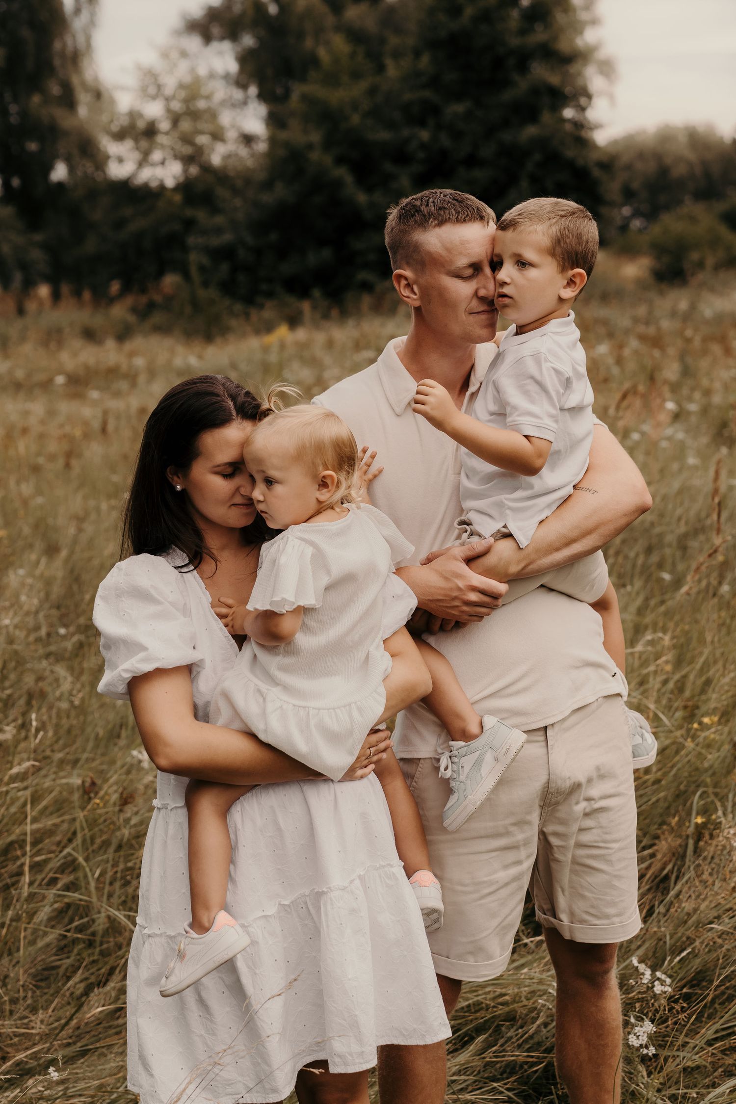 Family portrait in matching white outfits standing together in tall grass field.
