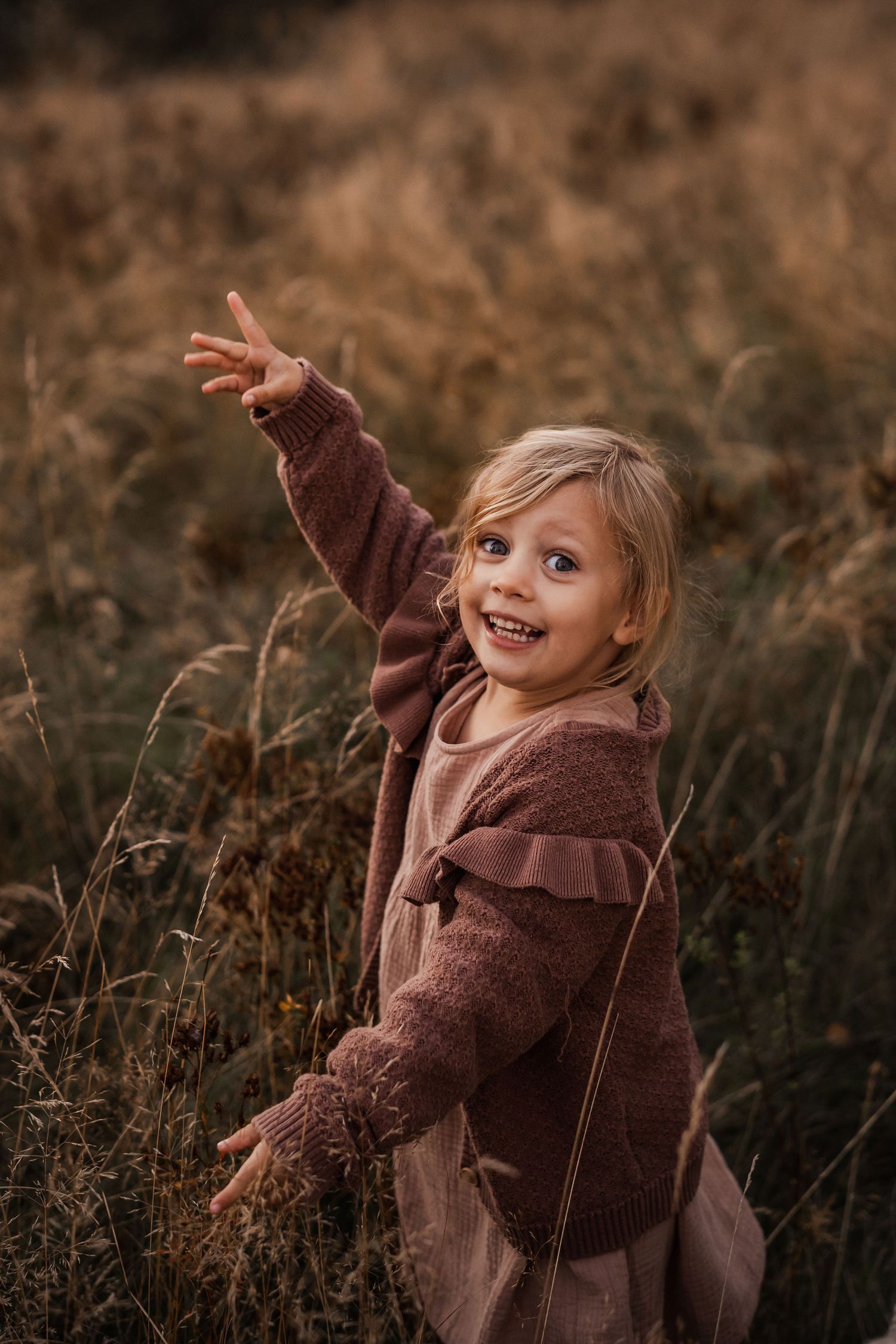 Joyful child in brown sweater plays in autumn field with arms outstretched.