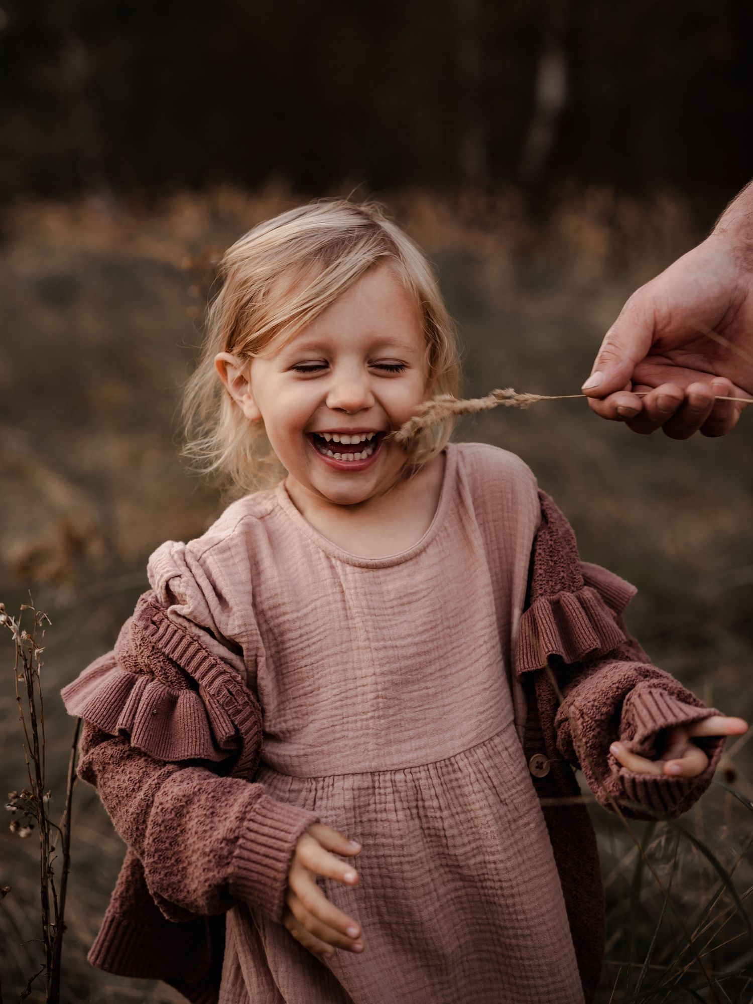 Small child laughs joyfully in a brown dress and sweater while playing in an autumn field.