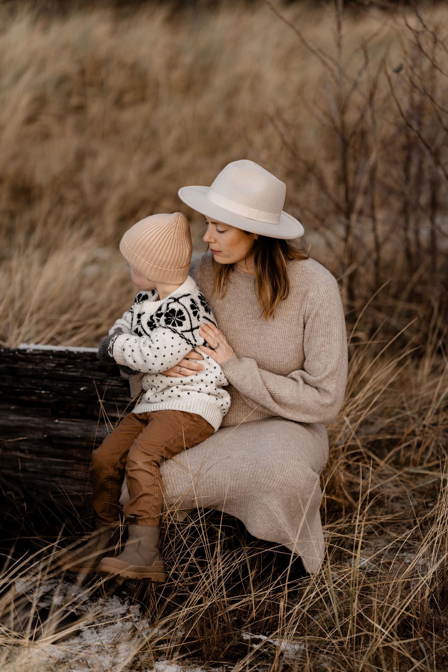 Tender moment between parent and child sitting on log wearing matching neutral knit sweaters.
