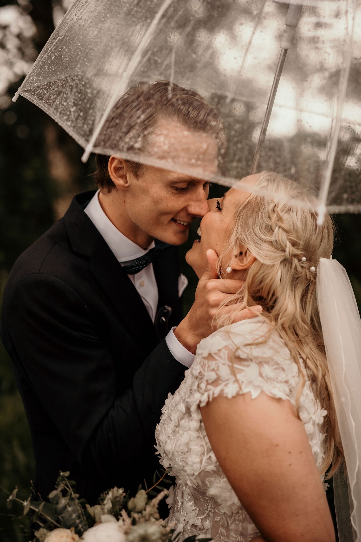 Romantic wedding couple sharing an intimate moment under a clear umbrella in the rain.