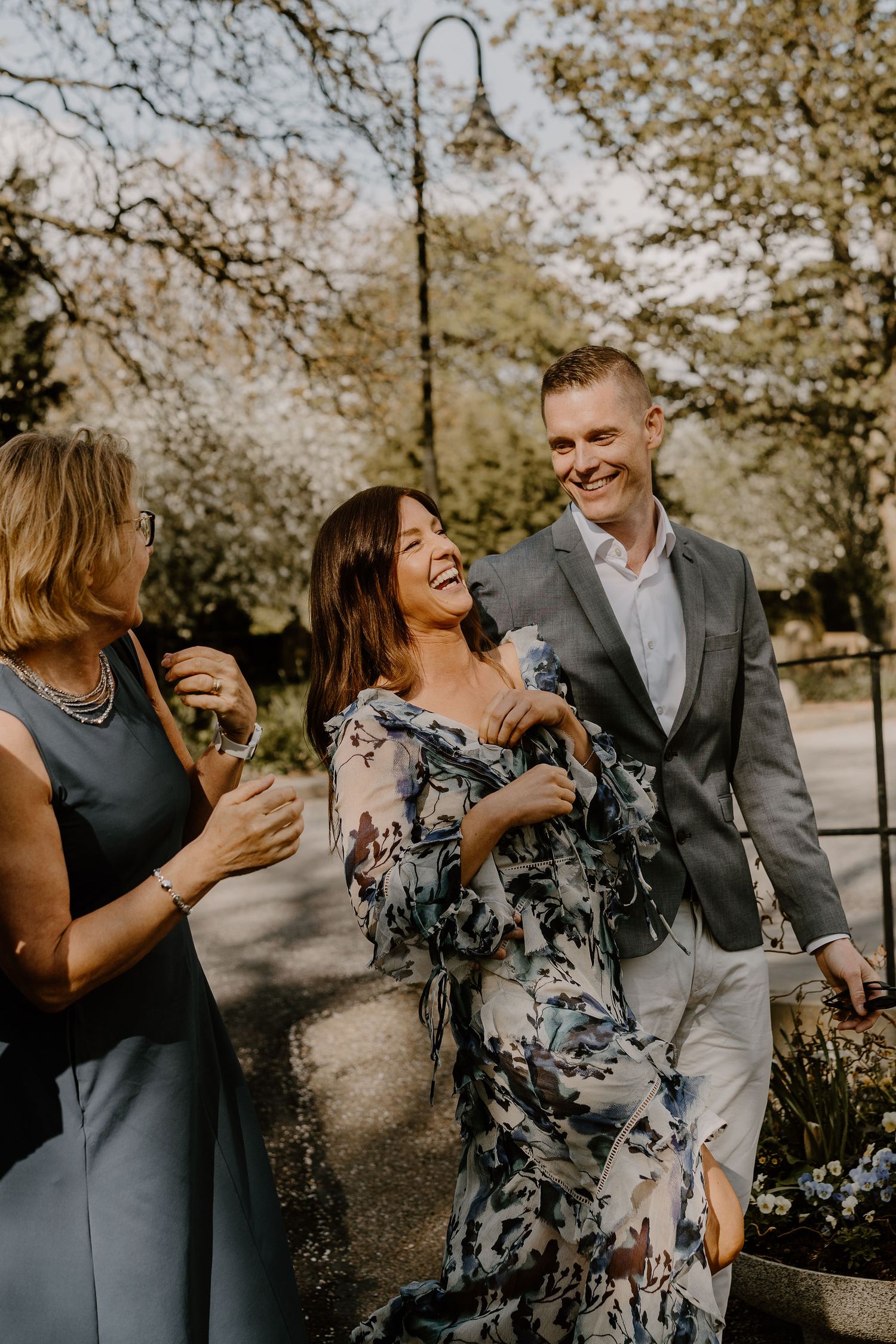 Group of people laughing together on tree-lined path during outdoor social gathering.