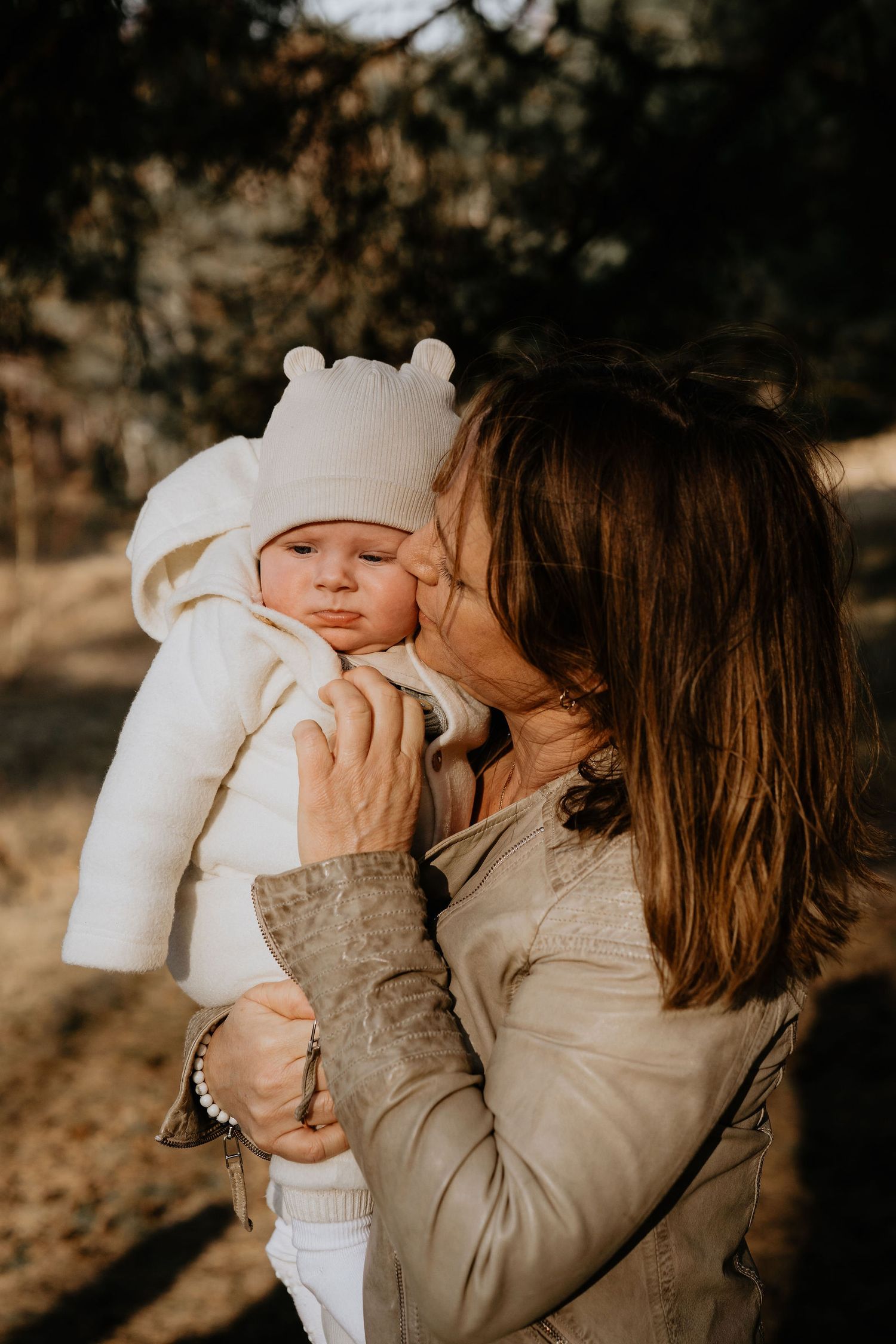 A tender moment captured at golden hour showing parent and baby in warm beige tones and a white bear ear hat.