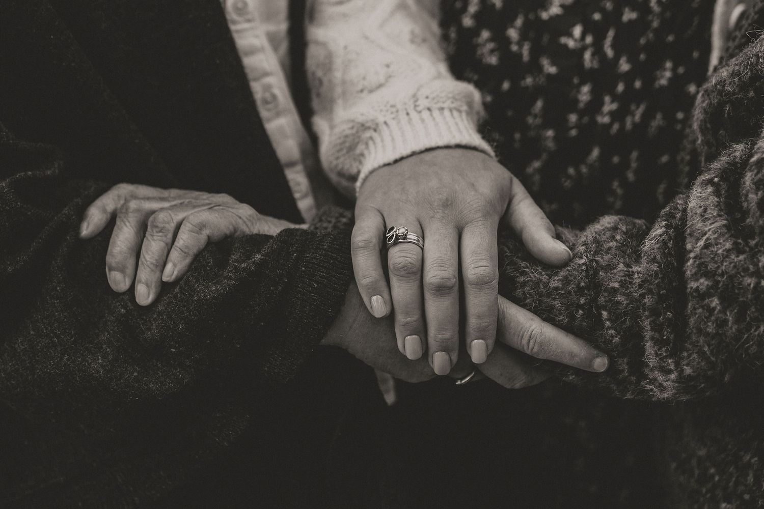 Black and white closeup of two hands clasped together showing an engagement or wedding ring.