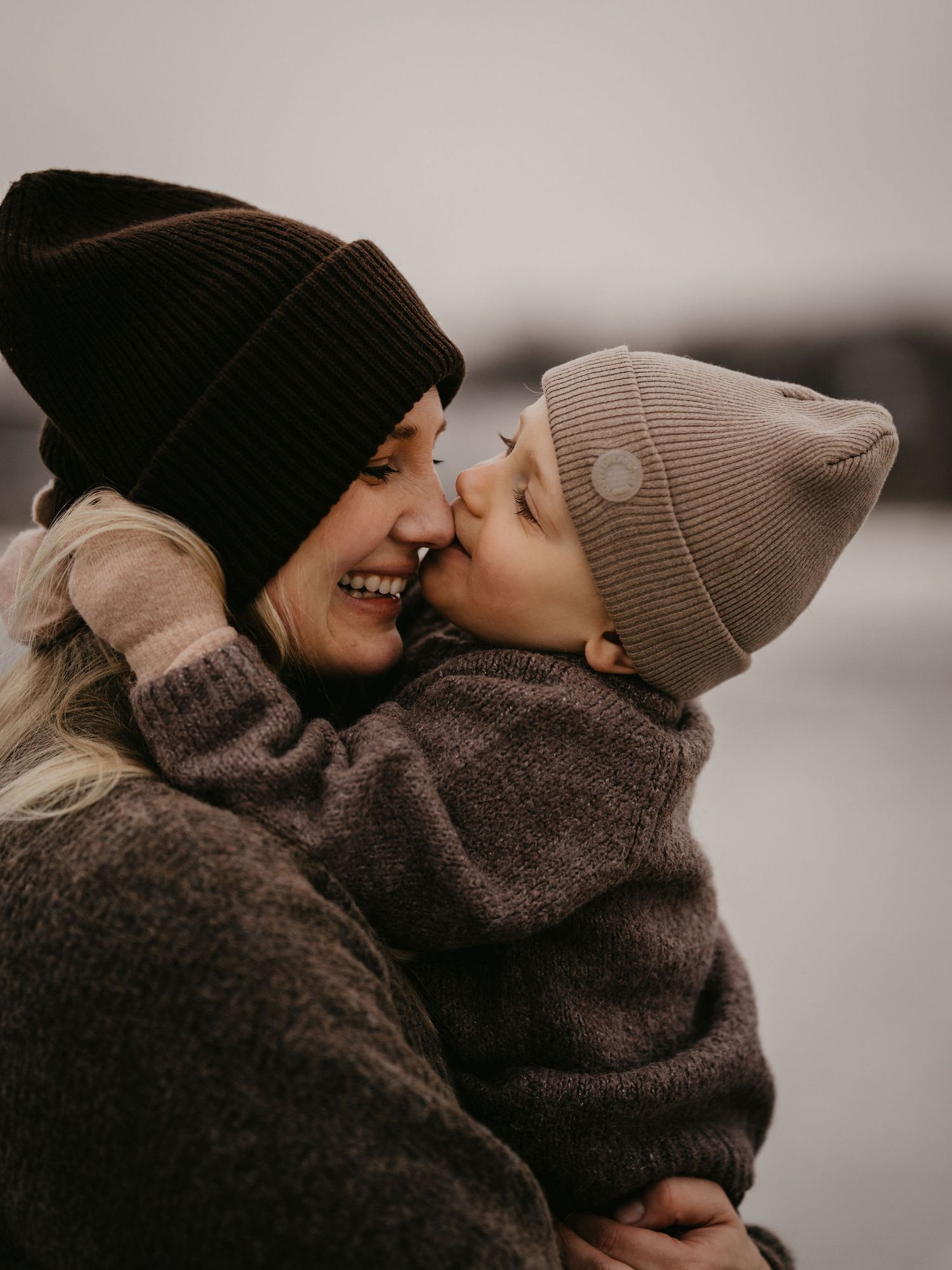 A touching moment captured between parent and child wearing knit beanies and cozy sweaters on an overcast day.