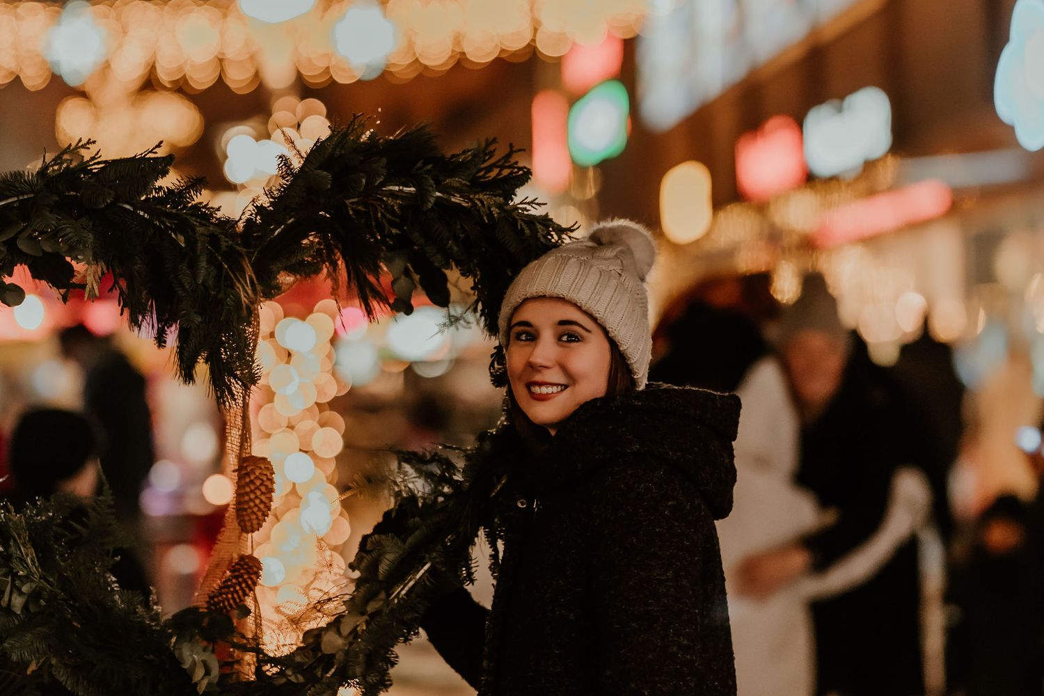Person wrapped in winter coat at night market with festive lights and decorations creating a warm holiday atmosphere.