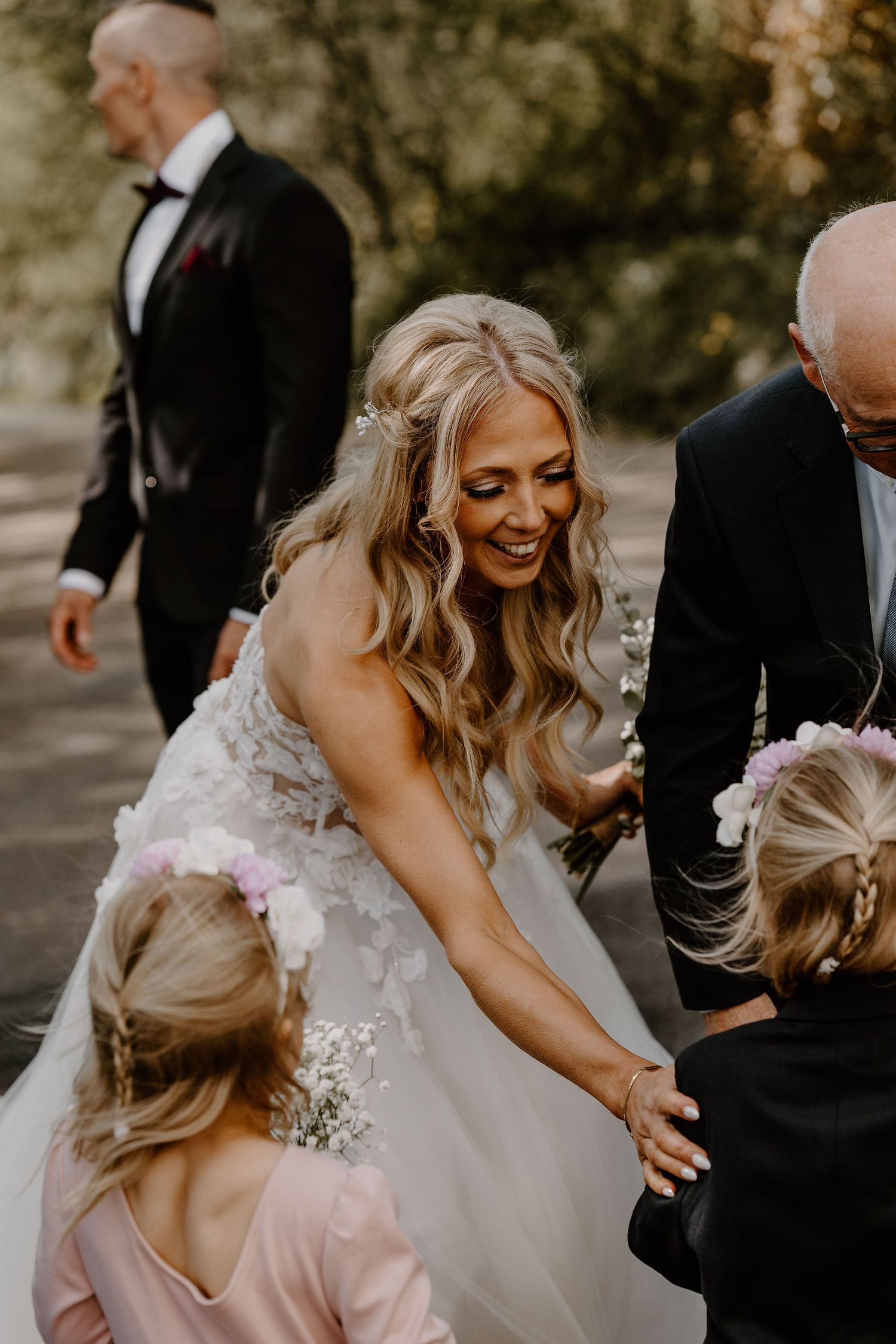 Joyful bride in a flowy white dress sharing a candid moment with children during outdoor wedding festivities.