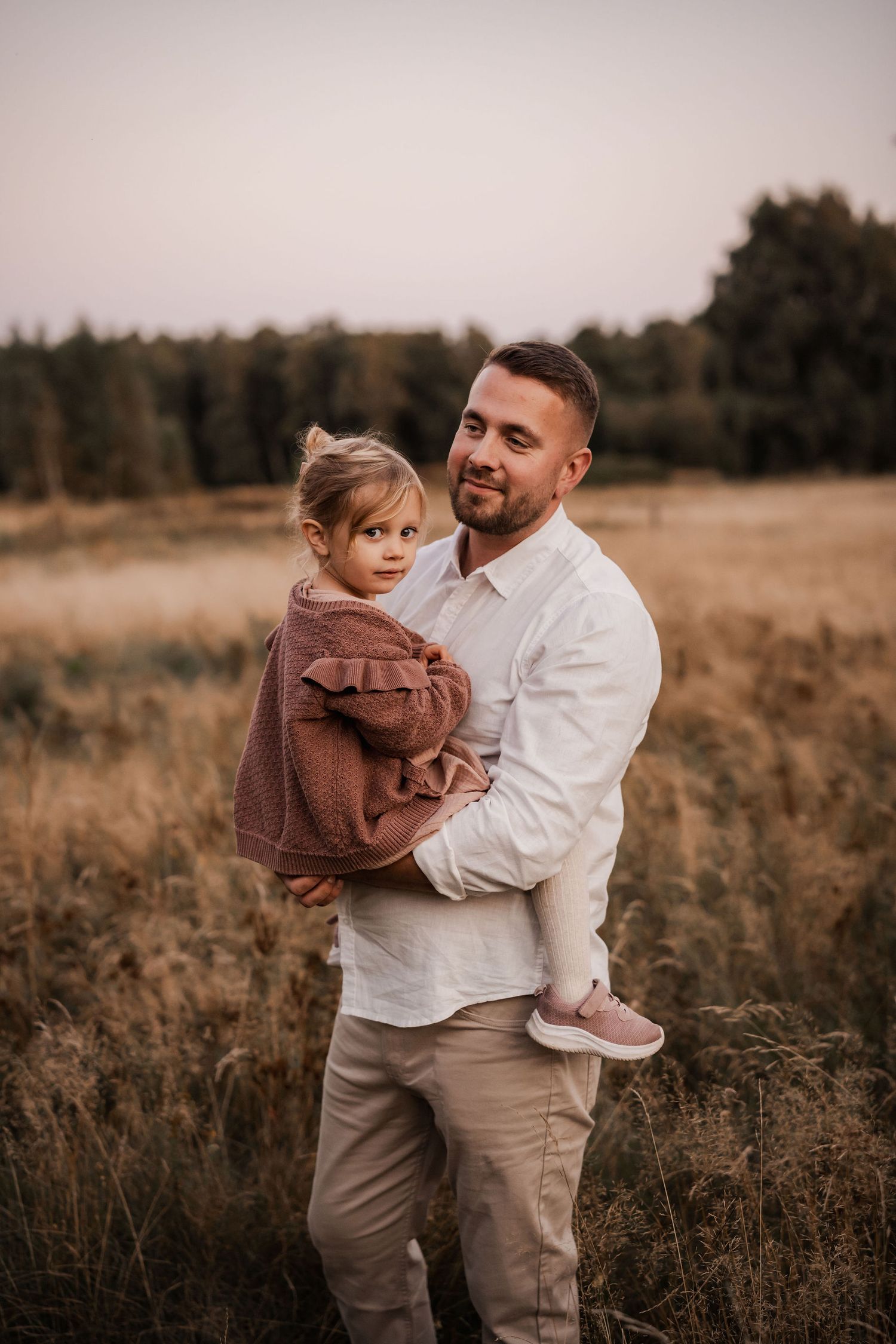 Family portrait in golden field at sunset showing tender moment between parent and child.