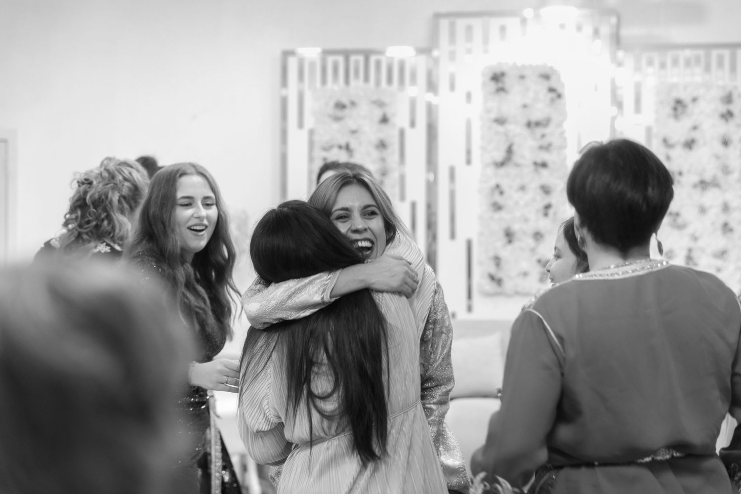 Black and white photo of women hugging and laughing at a social gathering indoors.